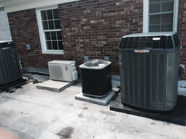Air conditioning units on a rooftop next to a brick building with windows.