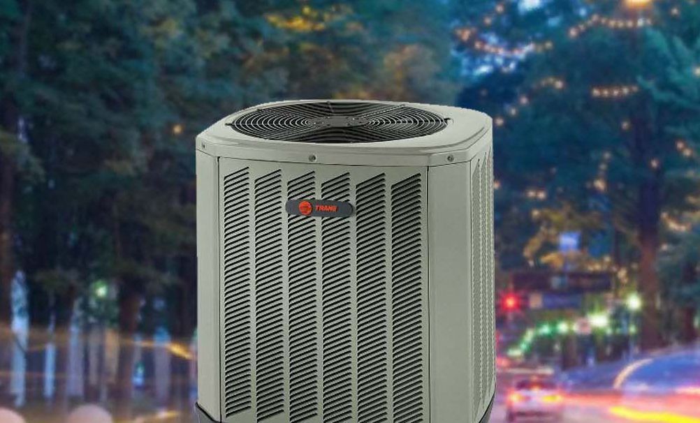 An air conditioning unit outdoors with a blurry street and lights in the background.