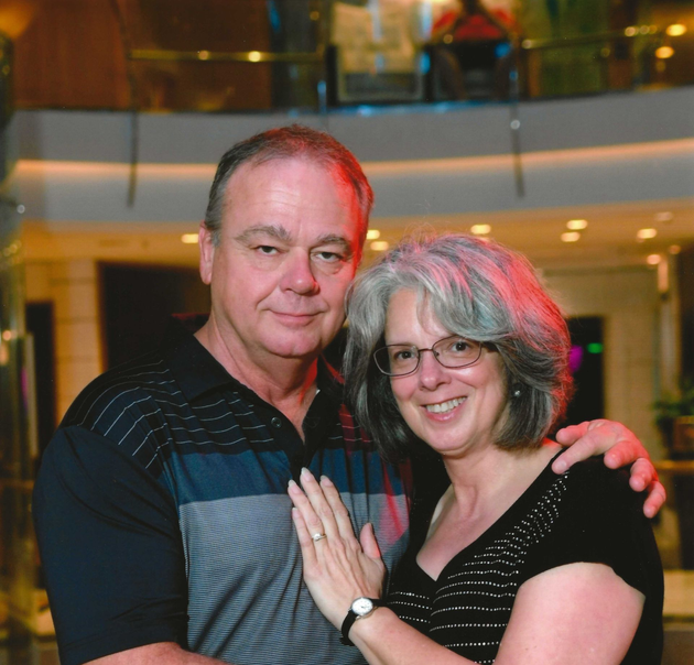 Smiling couple posing together indoors, with the woman’s hand on the man’s chest.