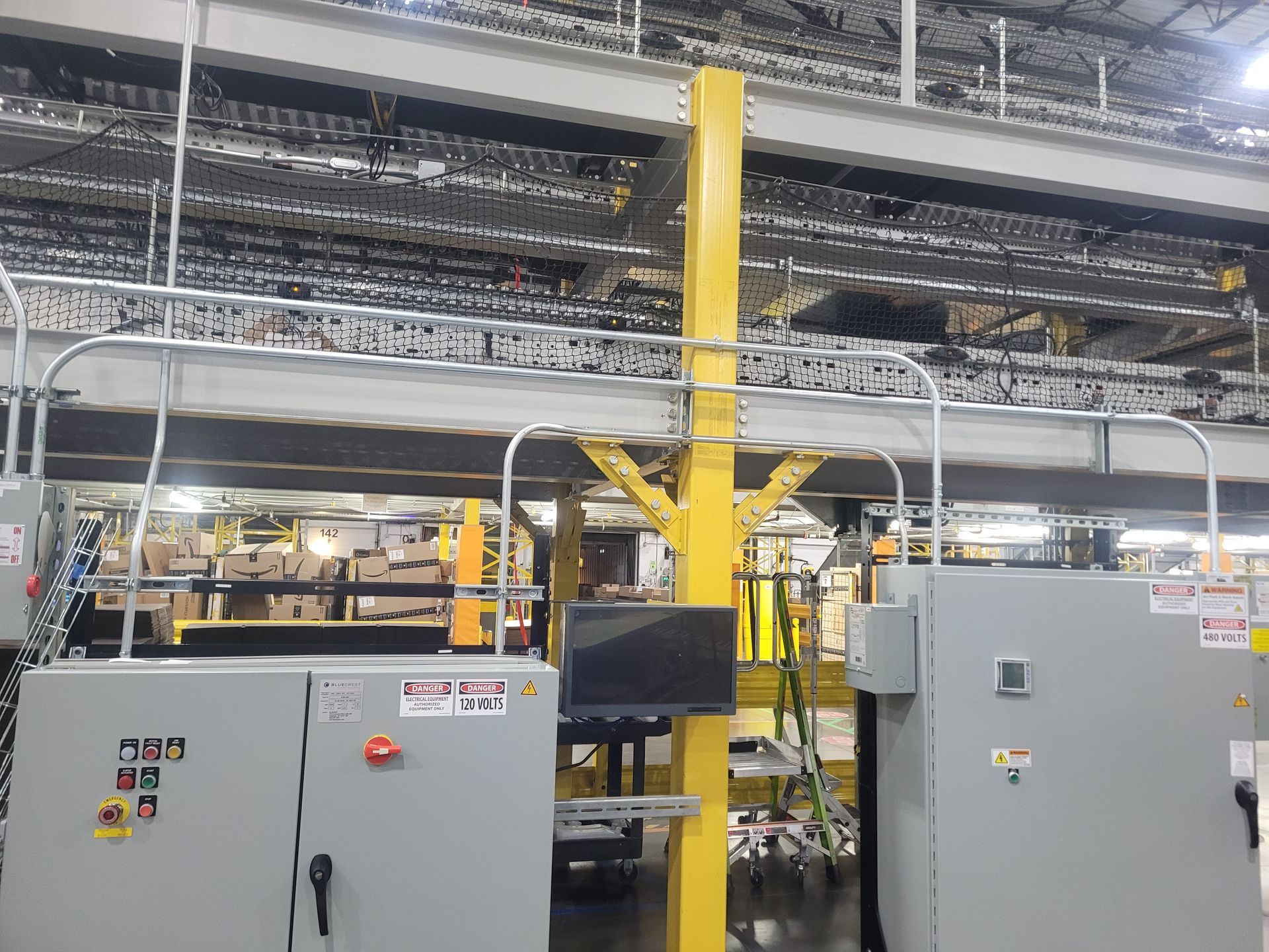 Industrial factory floor with machines and conveyor lines beneath overhead piping and lights
