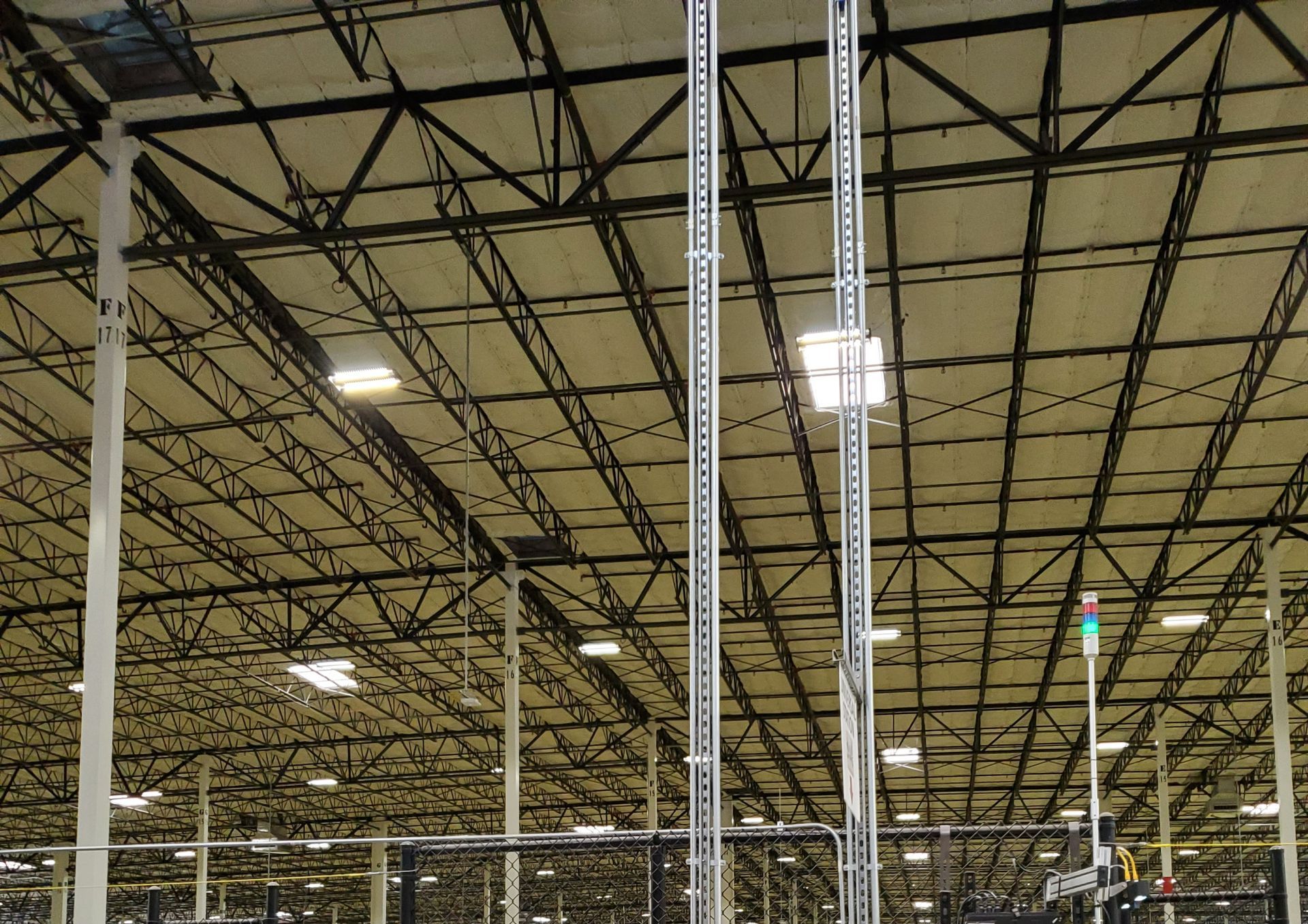 Interior of a large warehouse ceiling with exposed metal trusses and rows of overhead lights