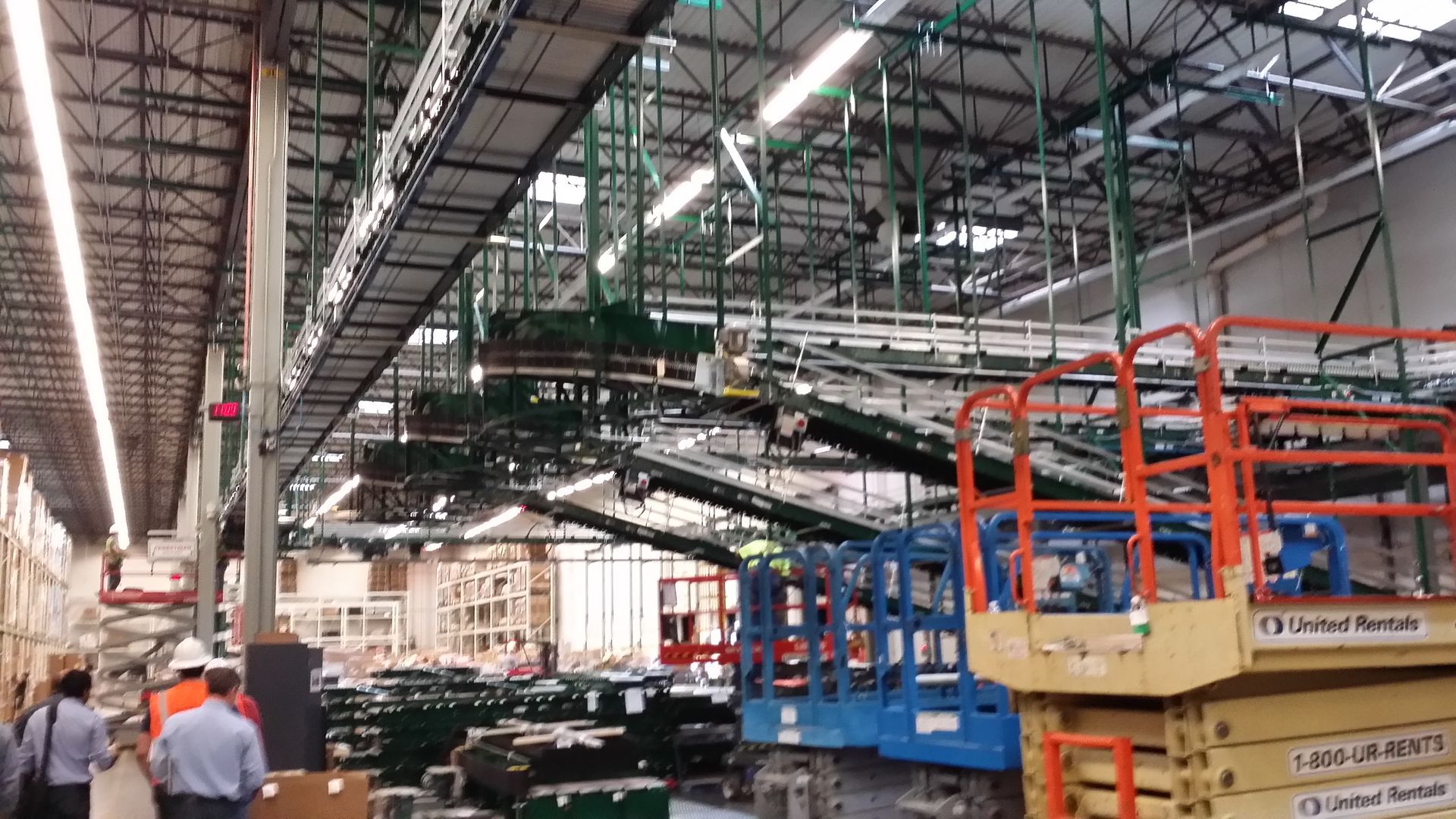 Industrial factory floor with assembly lines, overhead conveyors, and workers near orange lifts