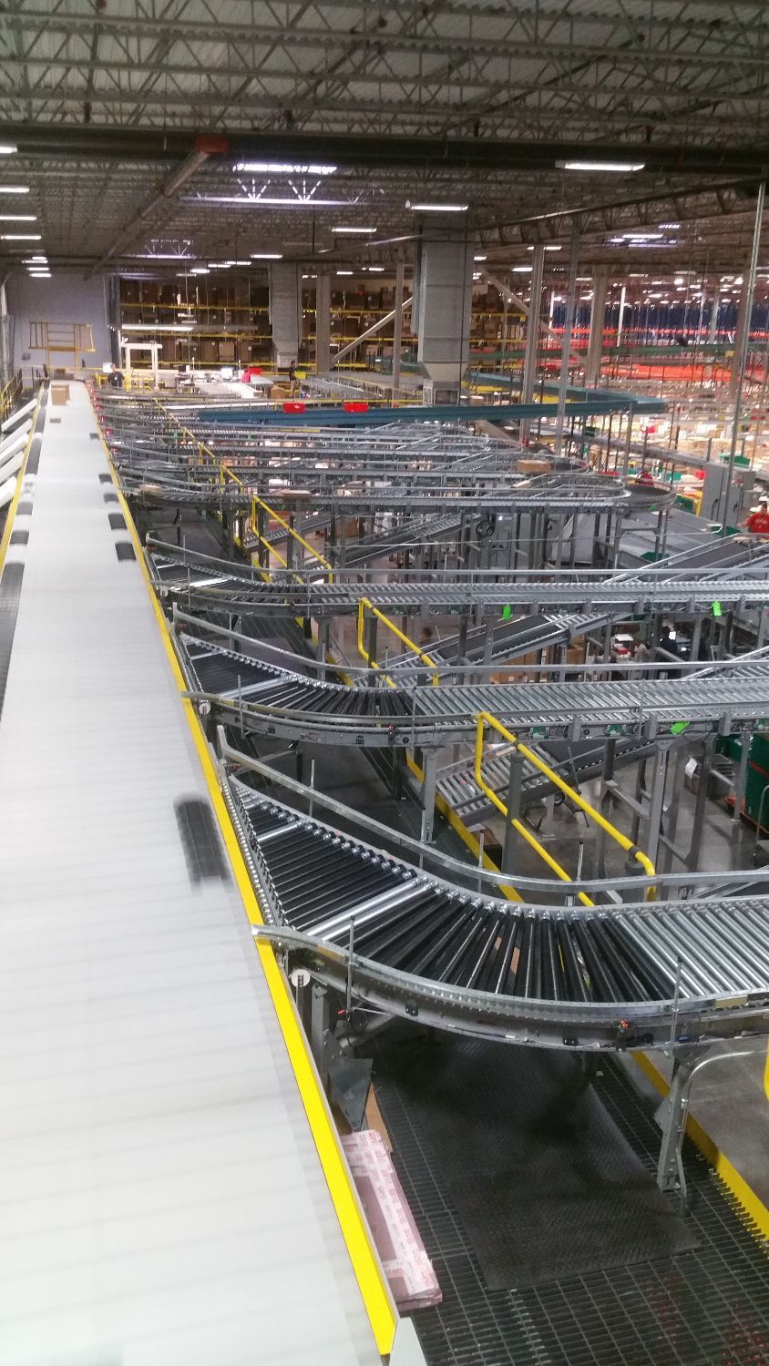 Warehouse conveyor system with silver rollers and yellow railings under bright industrial lighting