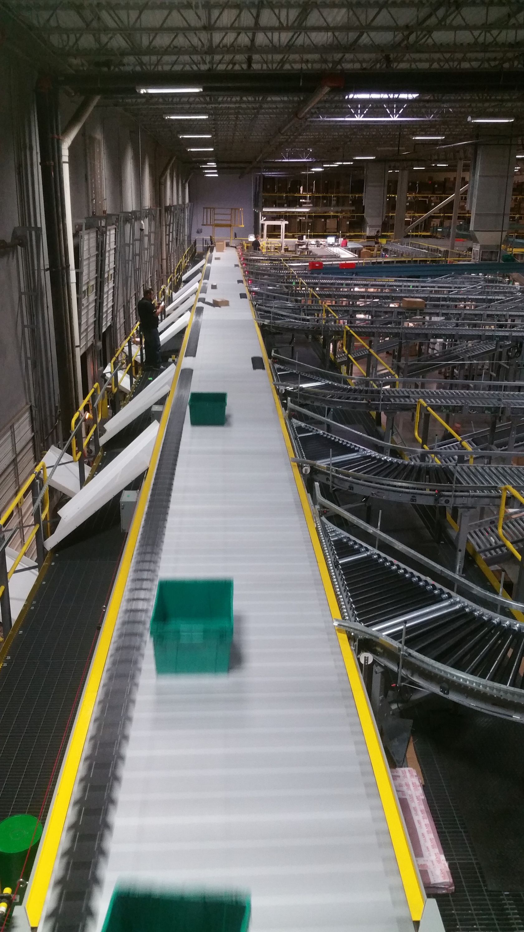 Industrial warehouse conveyor line with green bins and metal equipment under a high ceiling