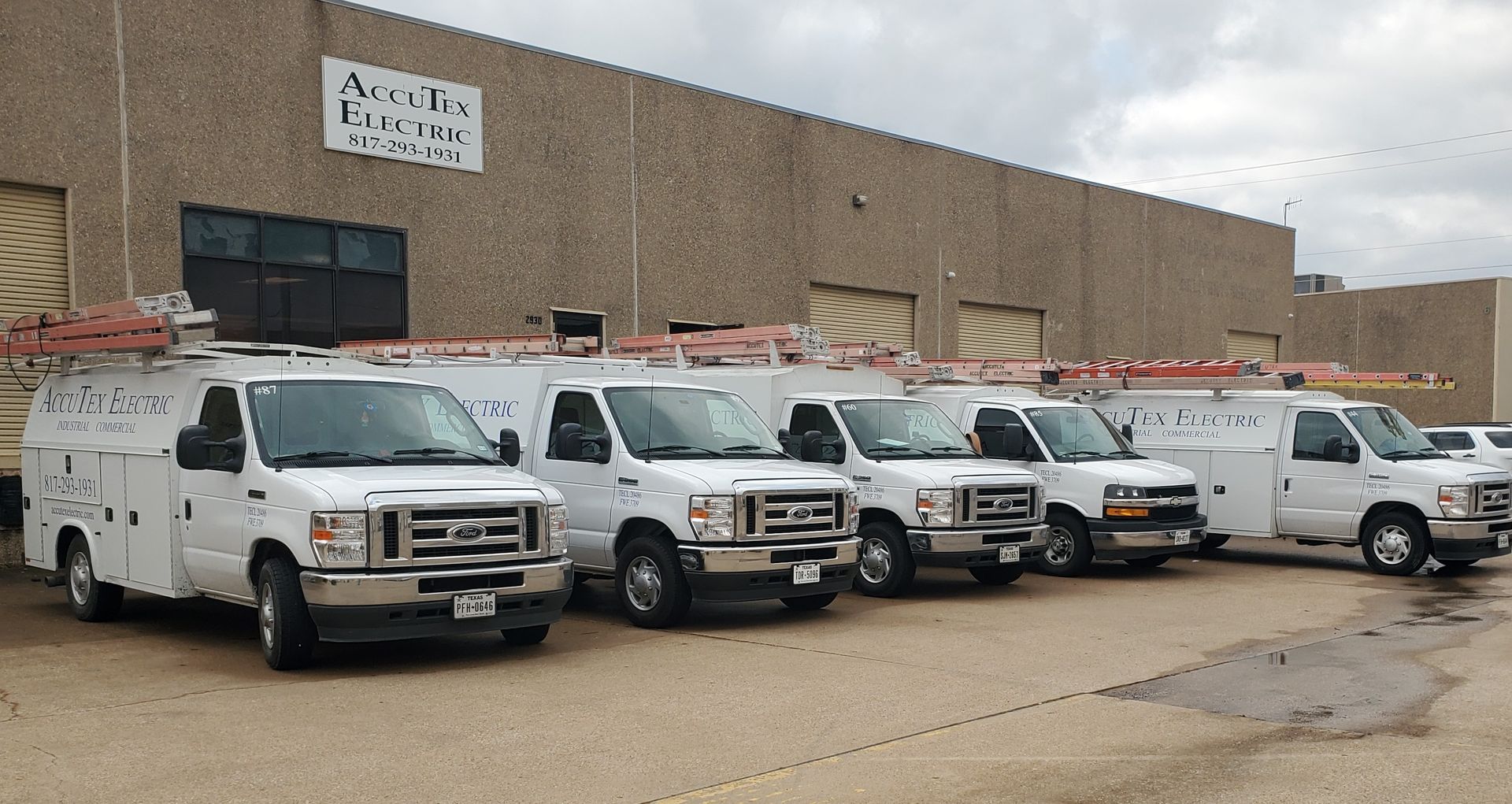 White utility vans parked outside a warehouse building on a cloudy day