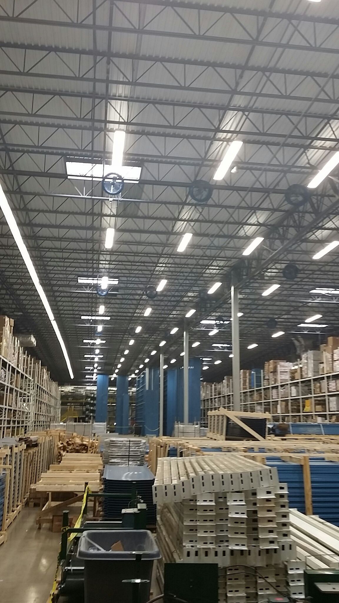 Warehouse interior with stacked pallets and metal beams under bright overhead lights