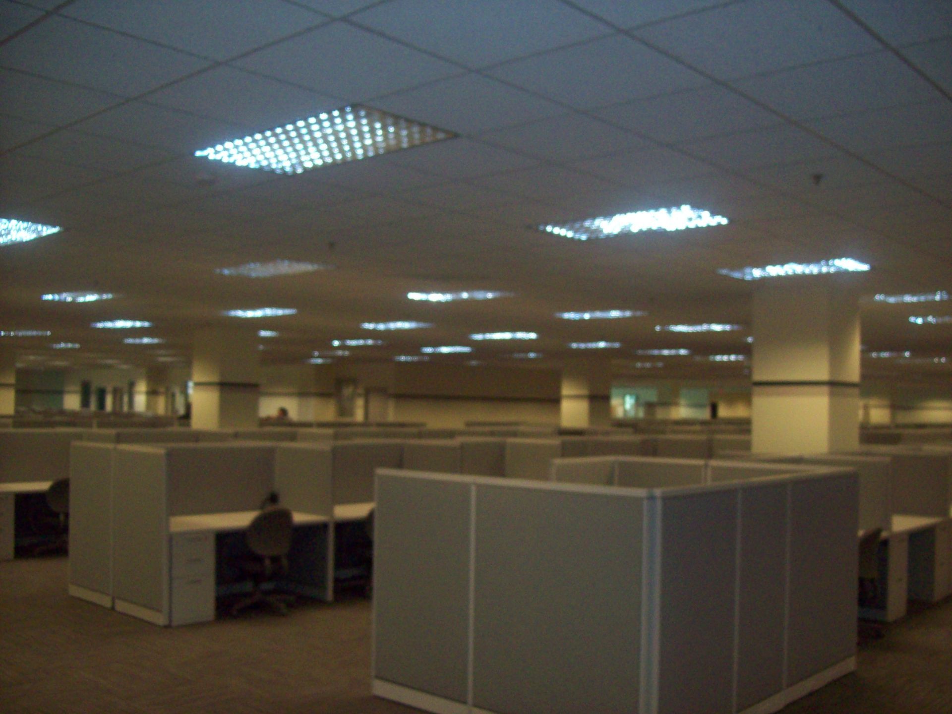 Dim office cubicles under fluorescent ceiling lights in a large open workspace.