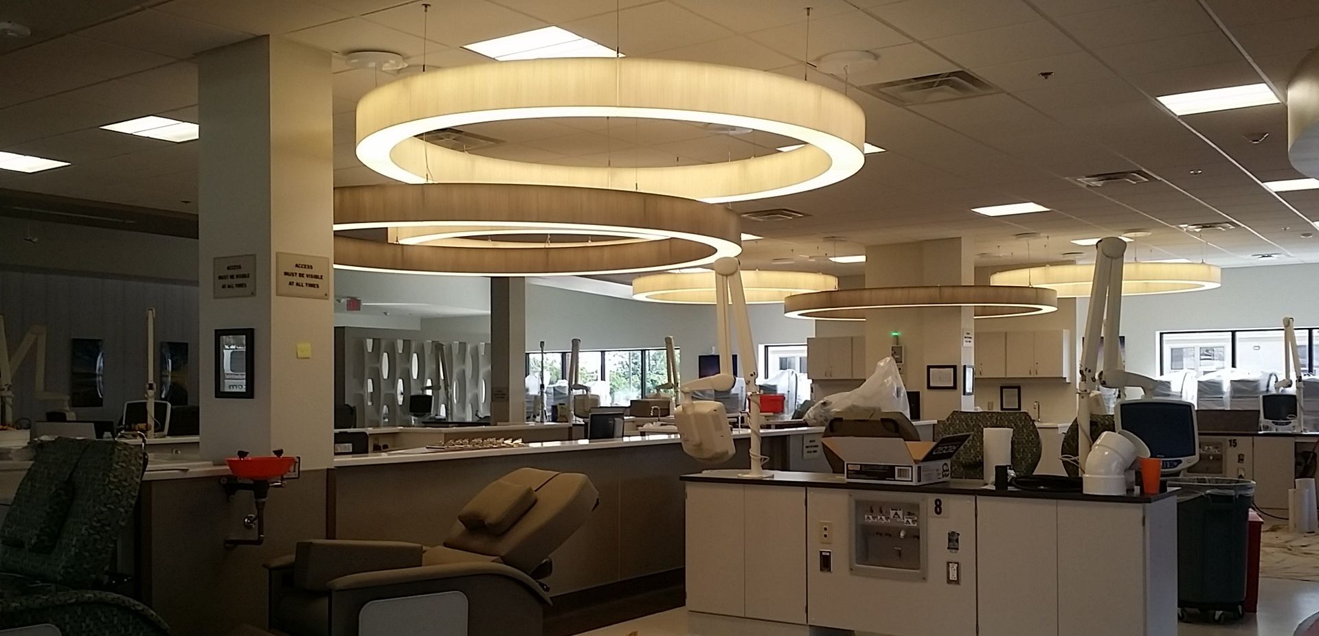 Modern office lounge with ring pendant lights, desks, computers, and people working in a bright open workspace