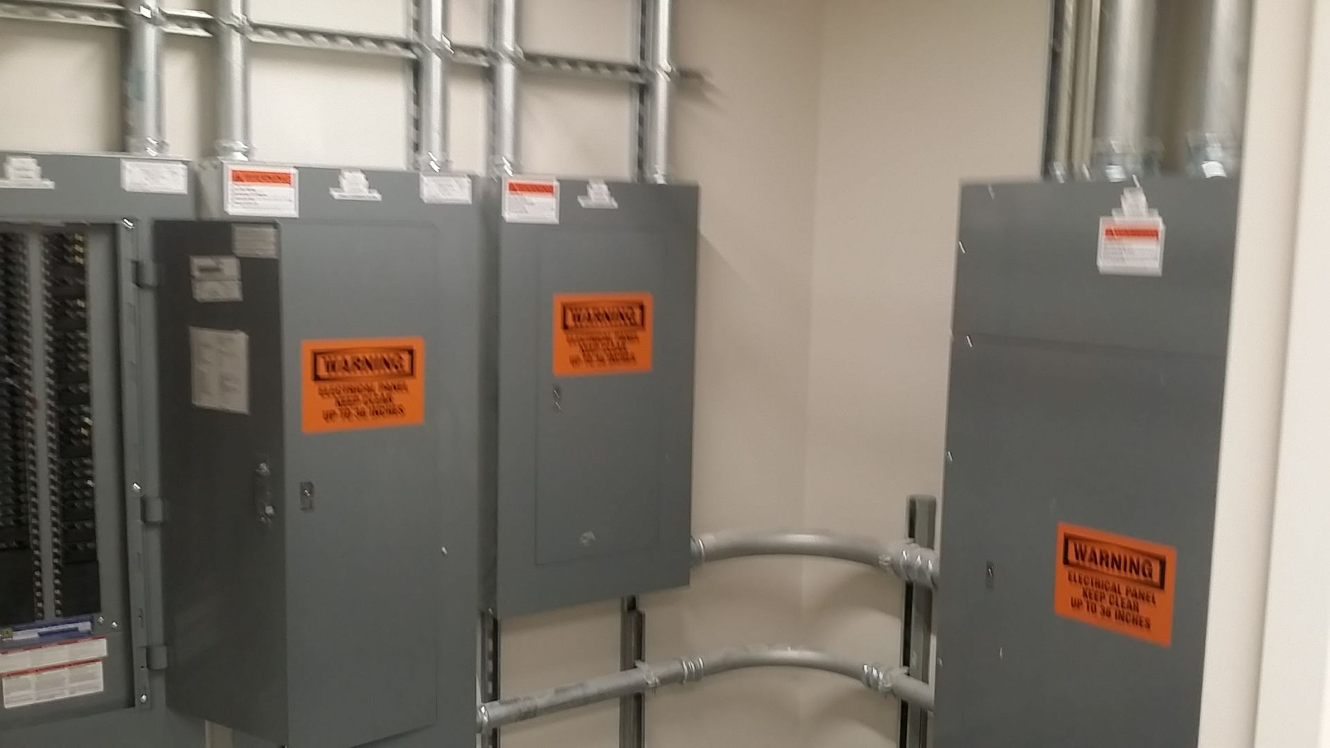 Gray electrical control panels with orange warning labels in an industrial room.