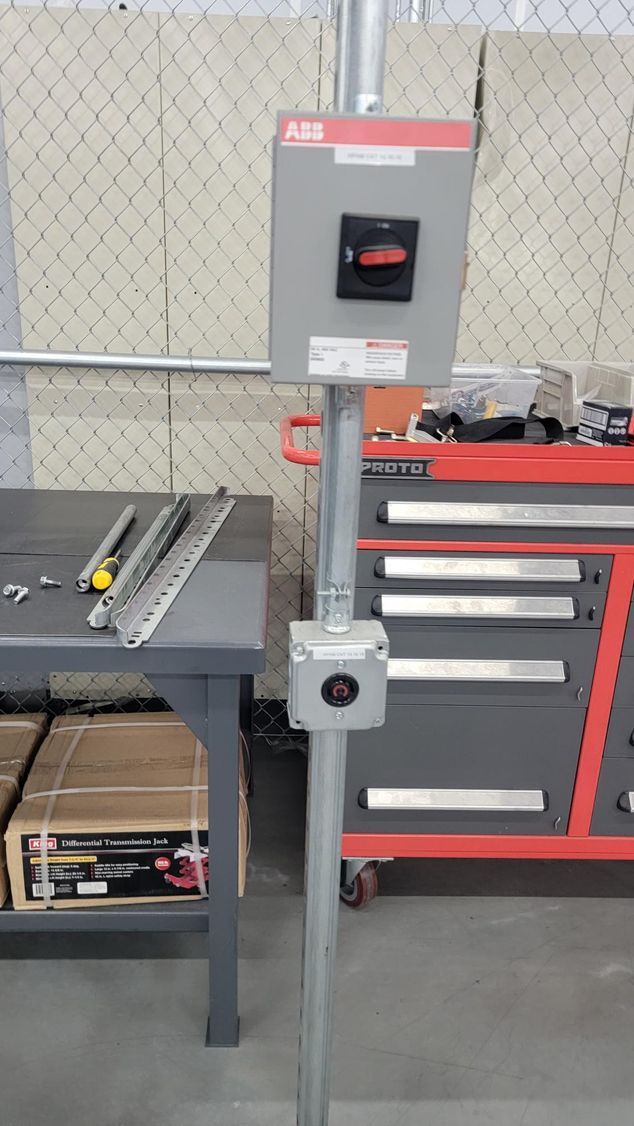 Industrial height gauge on a metal stand beside a workbench and red tool cabinet in a workshop.