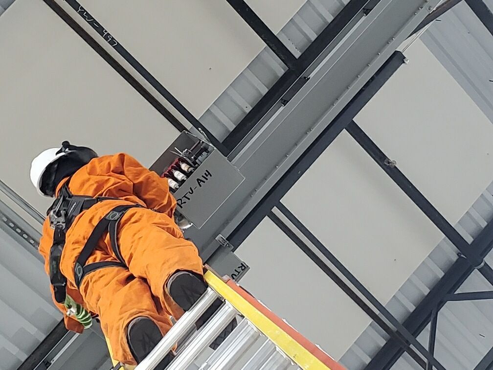 Worker in orange safety gear climbing a metal ladder indoors beneath steel beams.