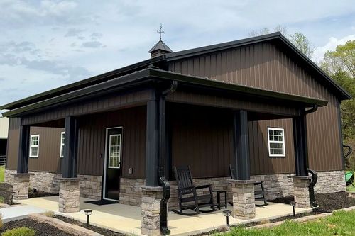 Dark brown cabin-style building with stone porch columns and a black rocking chair outside.