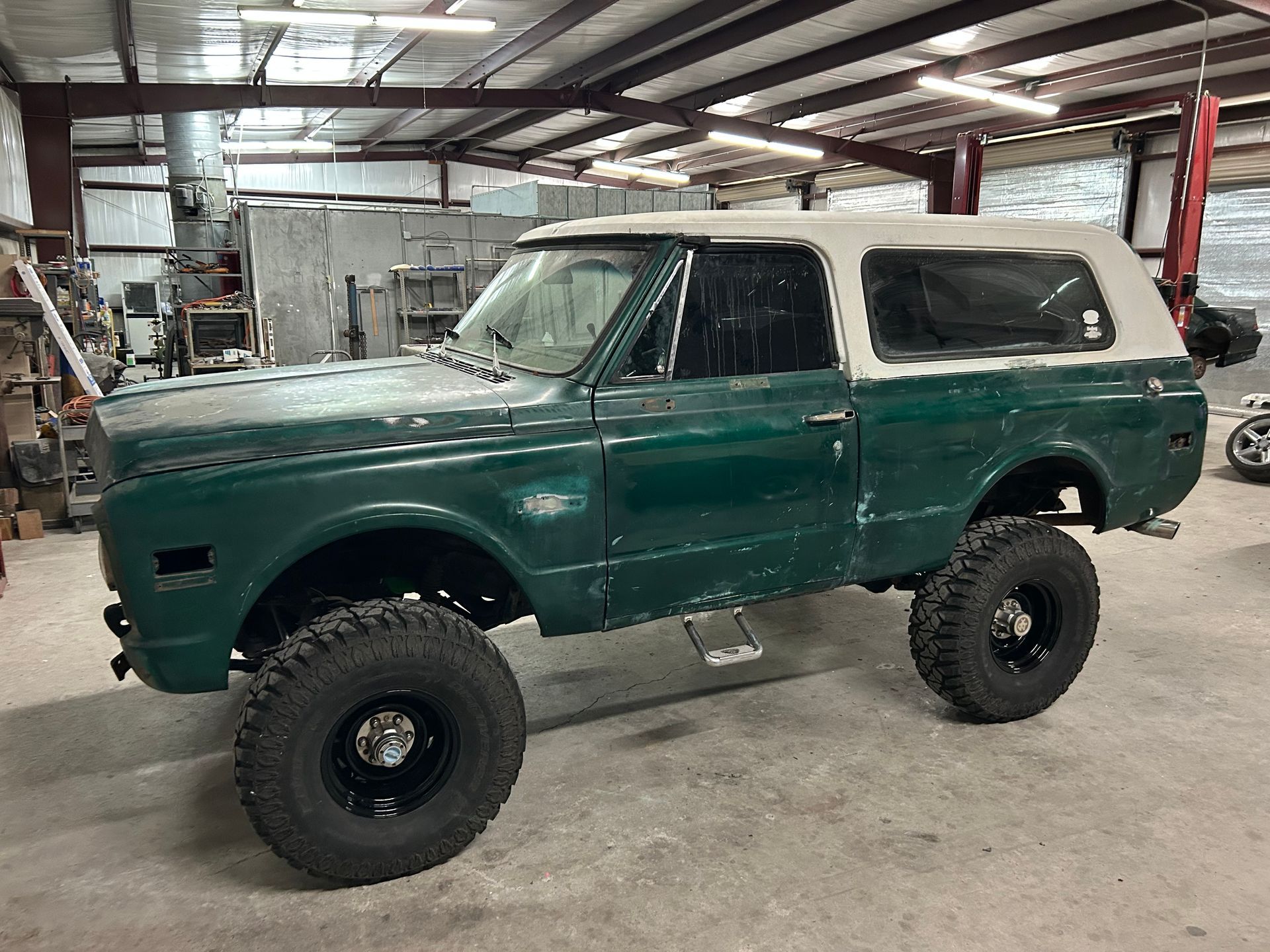 Green and white classic SUV with large black tires parked in a garage.