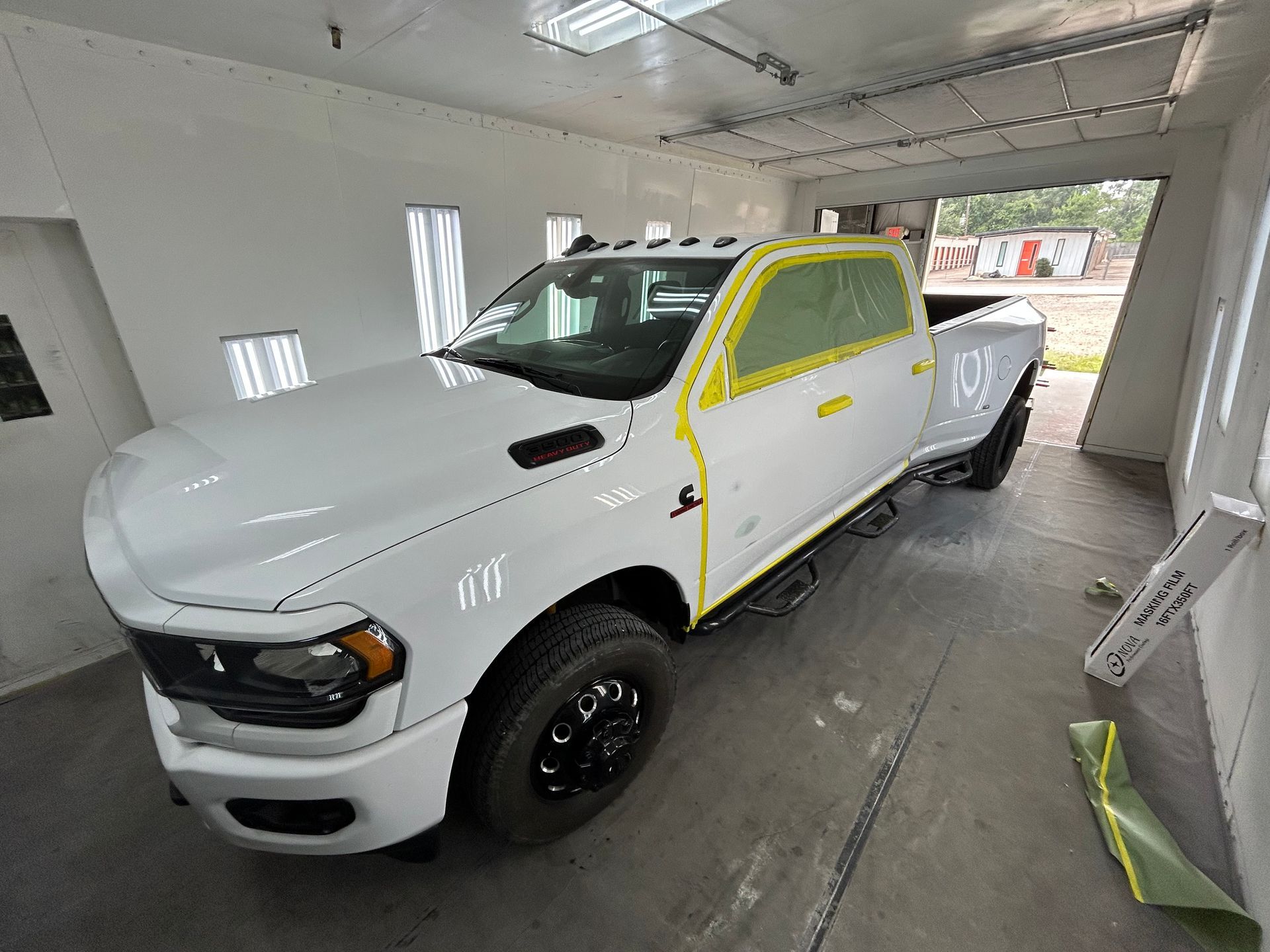 White Ram pickup truck being painted in a body shop paint booth with masking tape.