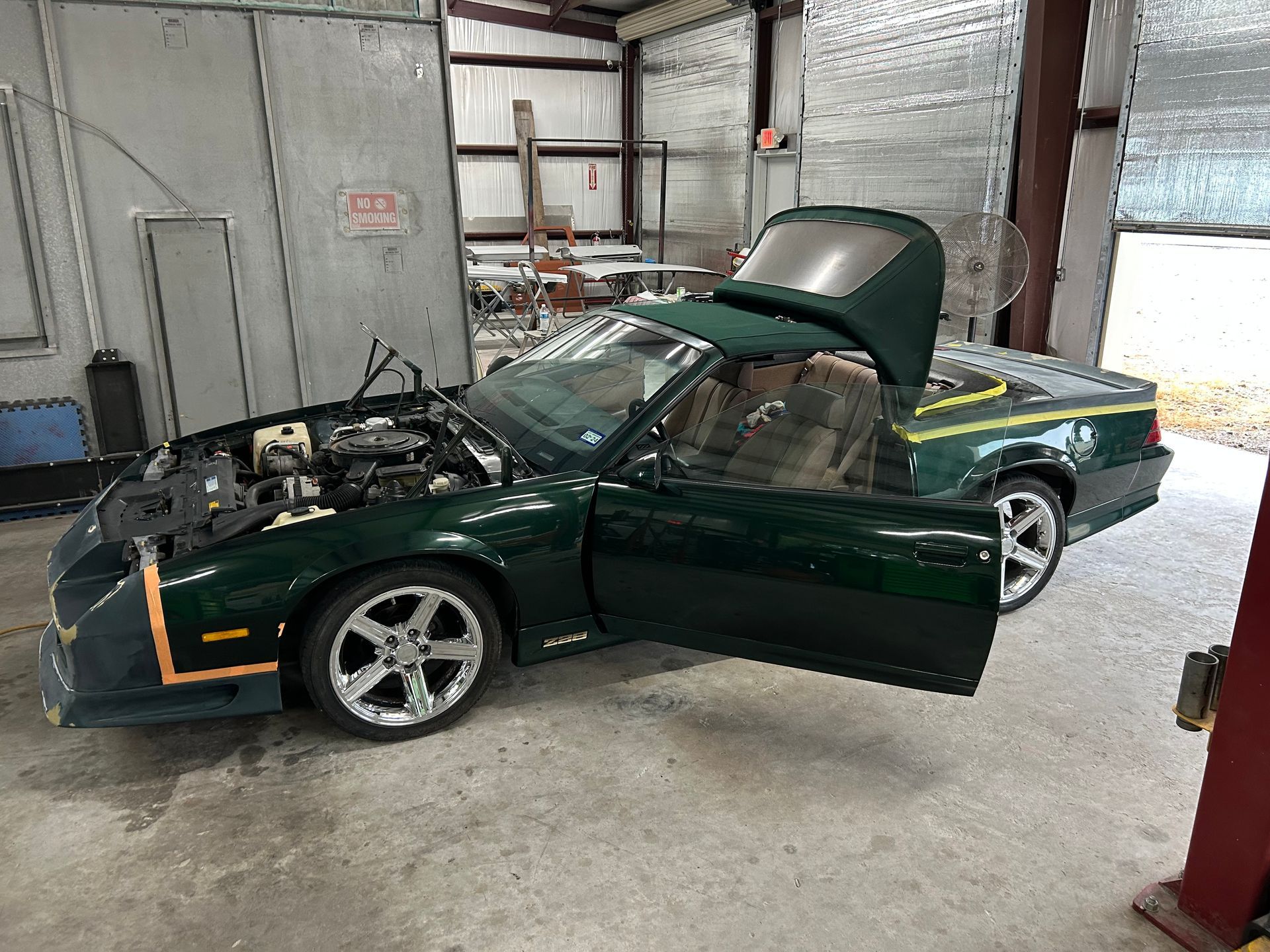 Green convertible car with hood open, in a garage with open door.
