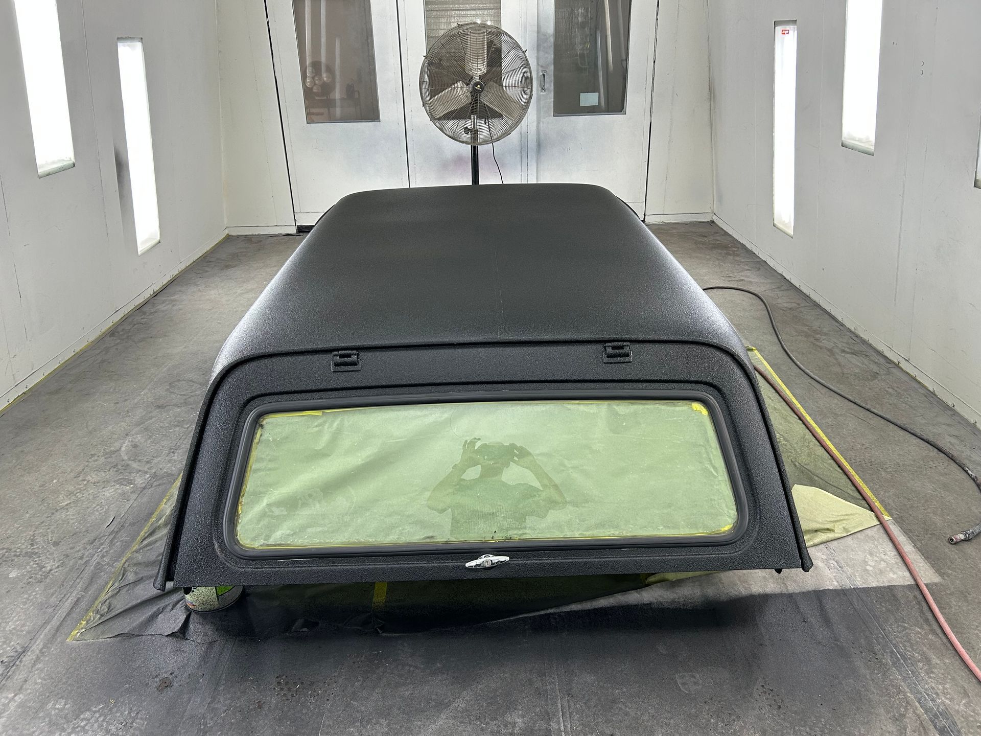 Truck bed topper, newly painted black, sits in a paint booth.