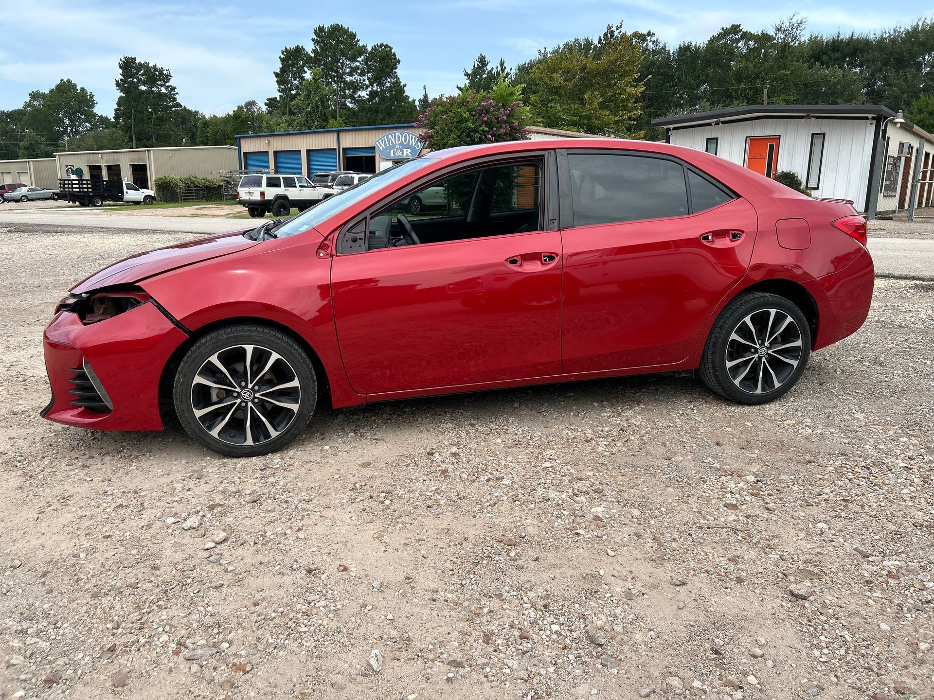 Red Toyota Corolla with front-end damage parked on gravel.