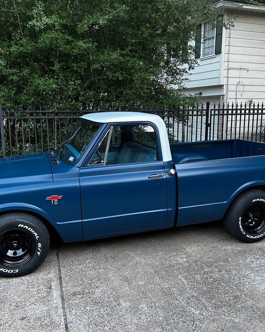 Blue classic pickup truck with a white roof, parked in front of a house.