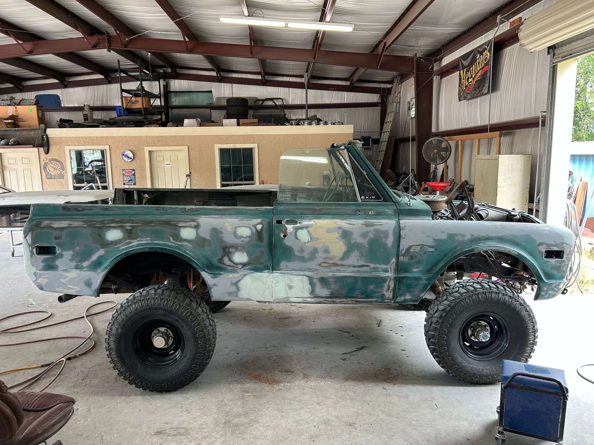 A lifted teal pickup truck undergoing restoration in a garage. It is missing a roof.