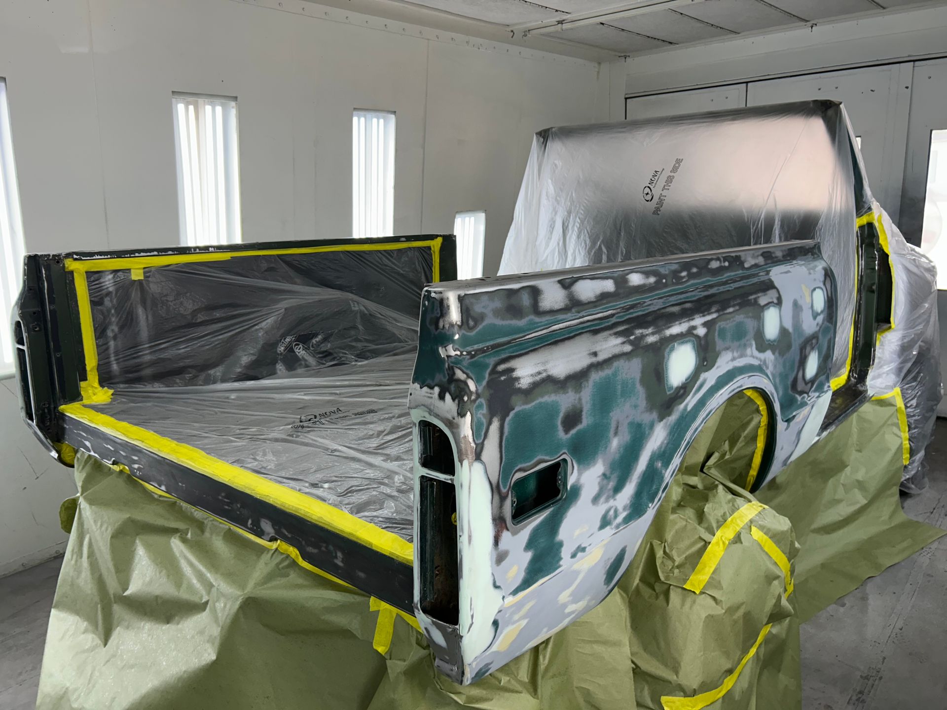 Truck bed in a paint booth, prepped for painting with masking tape and coverings.