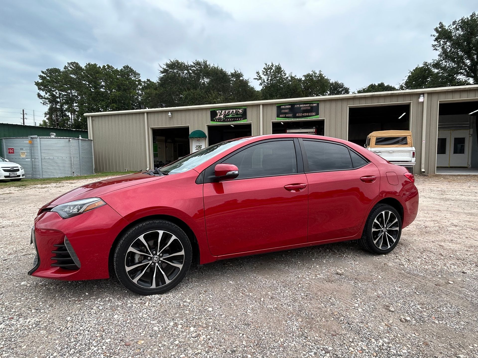 Red Toyota Corolla sedan parked in front of an auto shop.