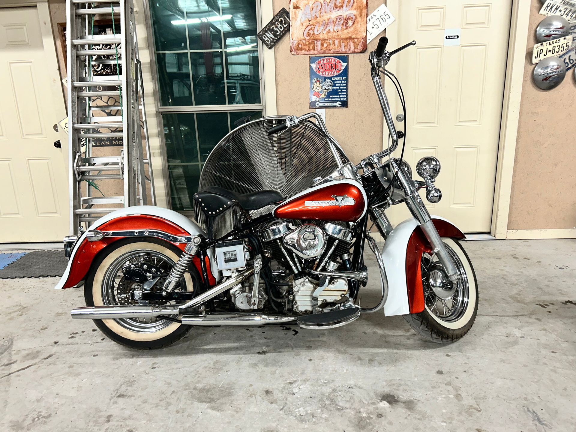 Red and white Harley Davidson motorcycle with ape hanger handlebars in a garage.