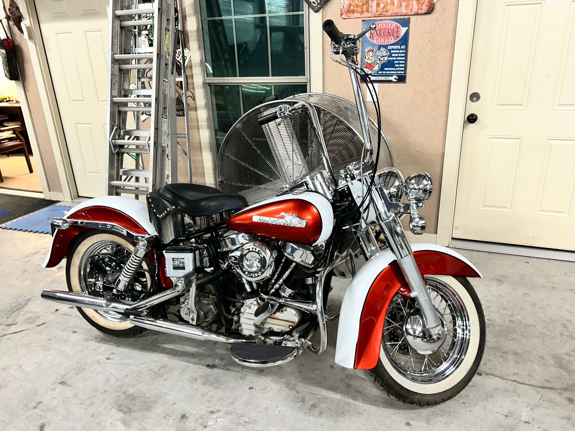 Red and white vintage Harley Davidson motorcycle with chrome accents, parked in a garage.