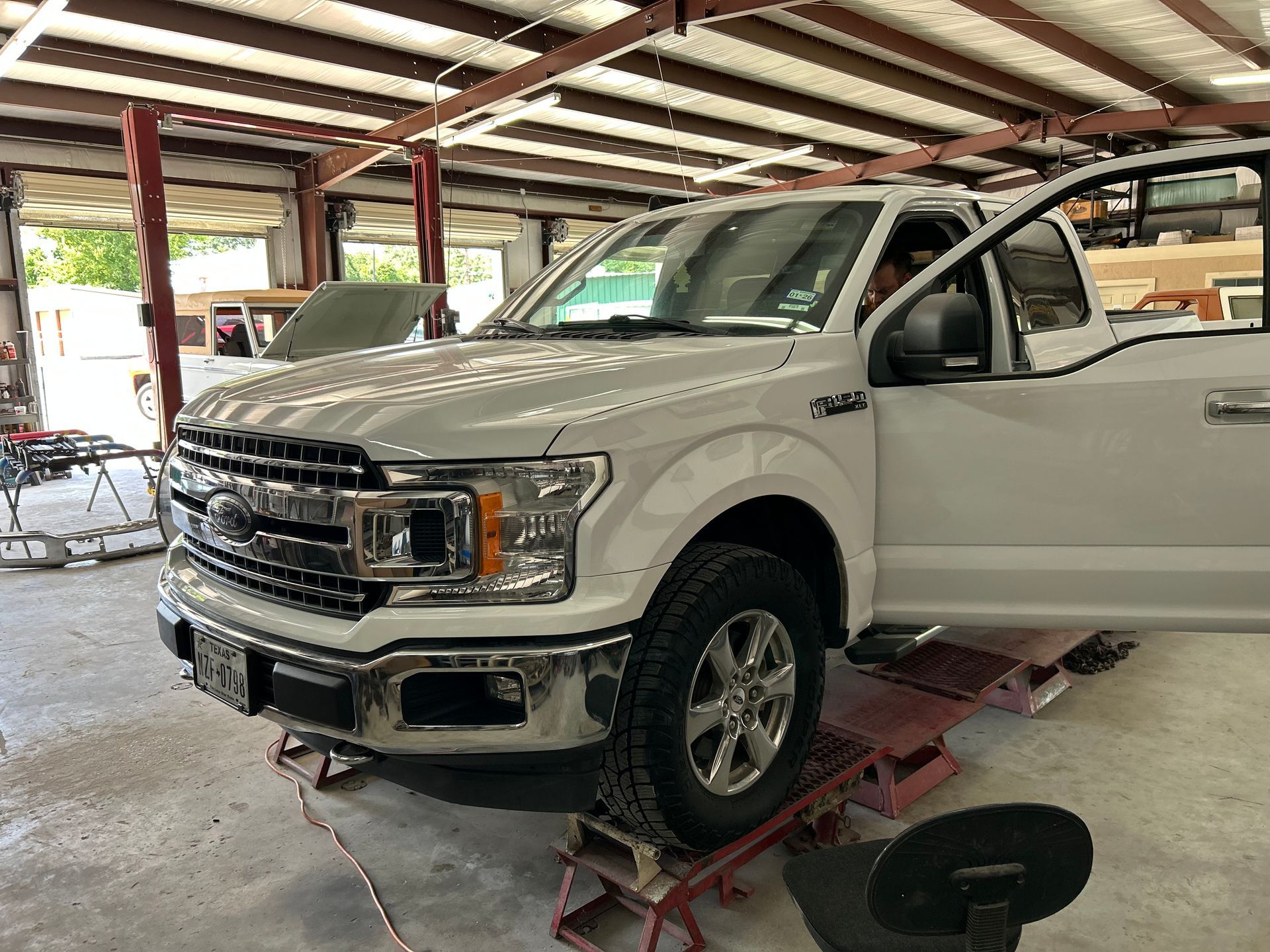 White Ford F-150 truck in a repair shop, door open, parked on red ramps.