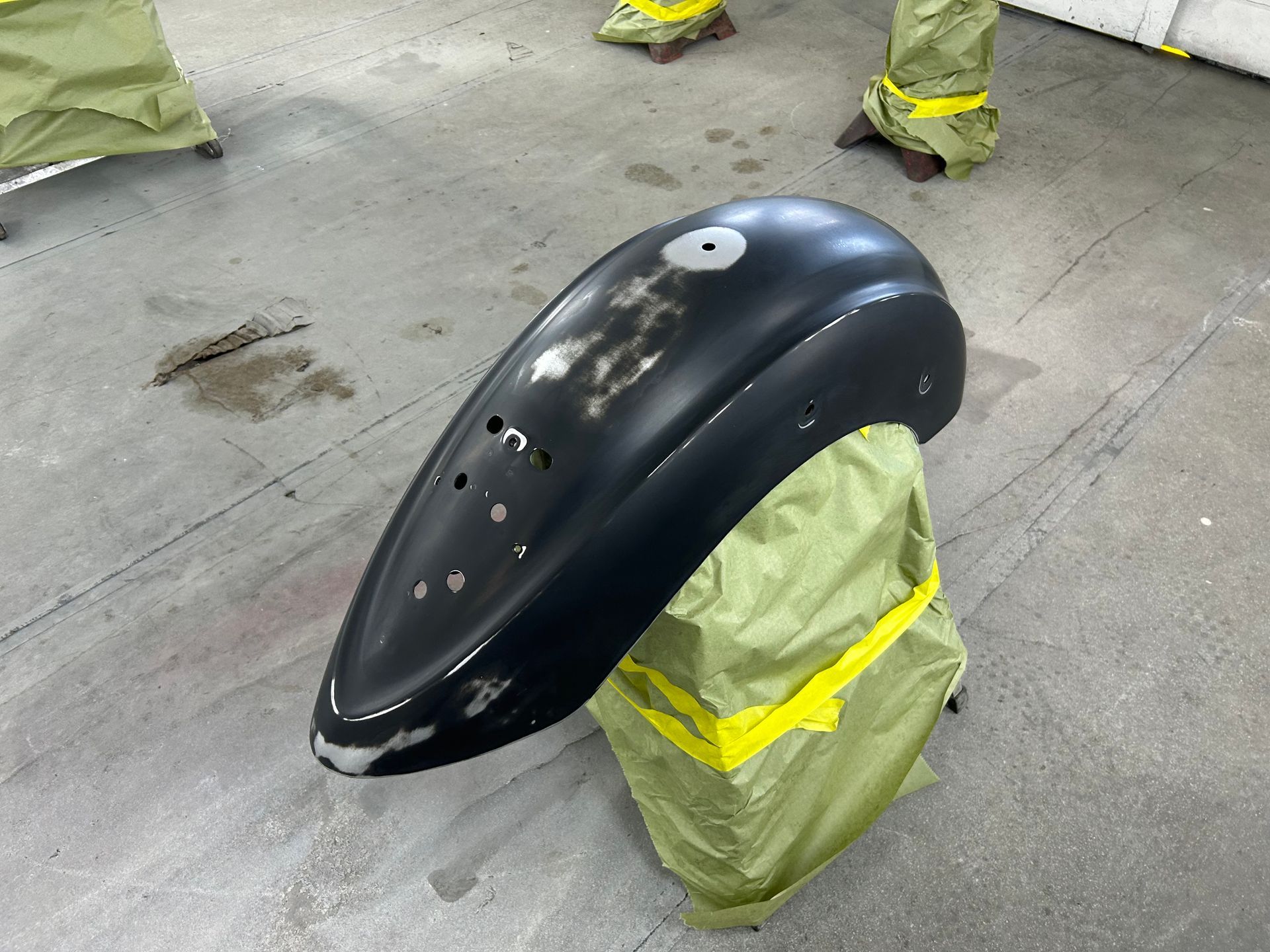 Black car fender on a yellow-taped stand, prepared for repair.