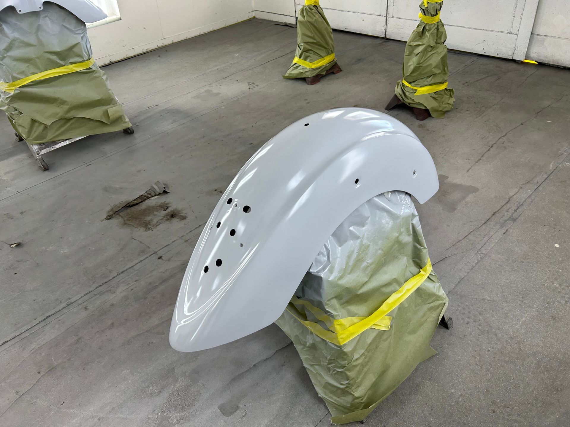 Motorcycle fender, freshly painted light gray, in a spray booth.