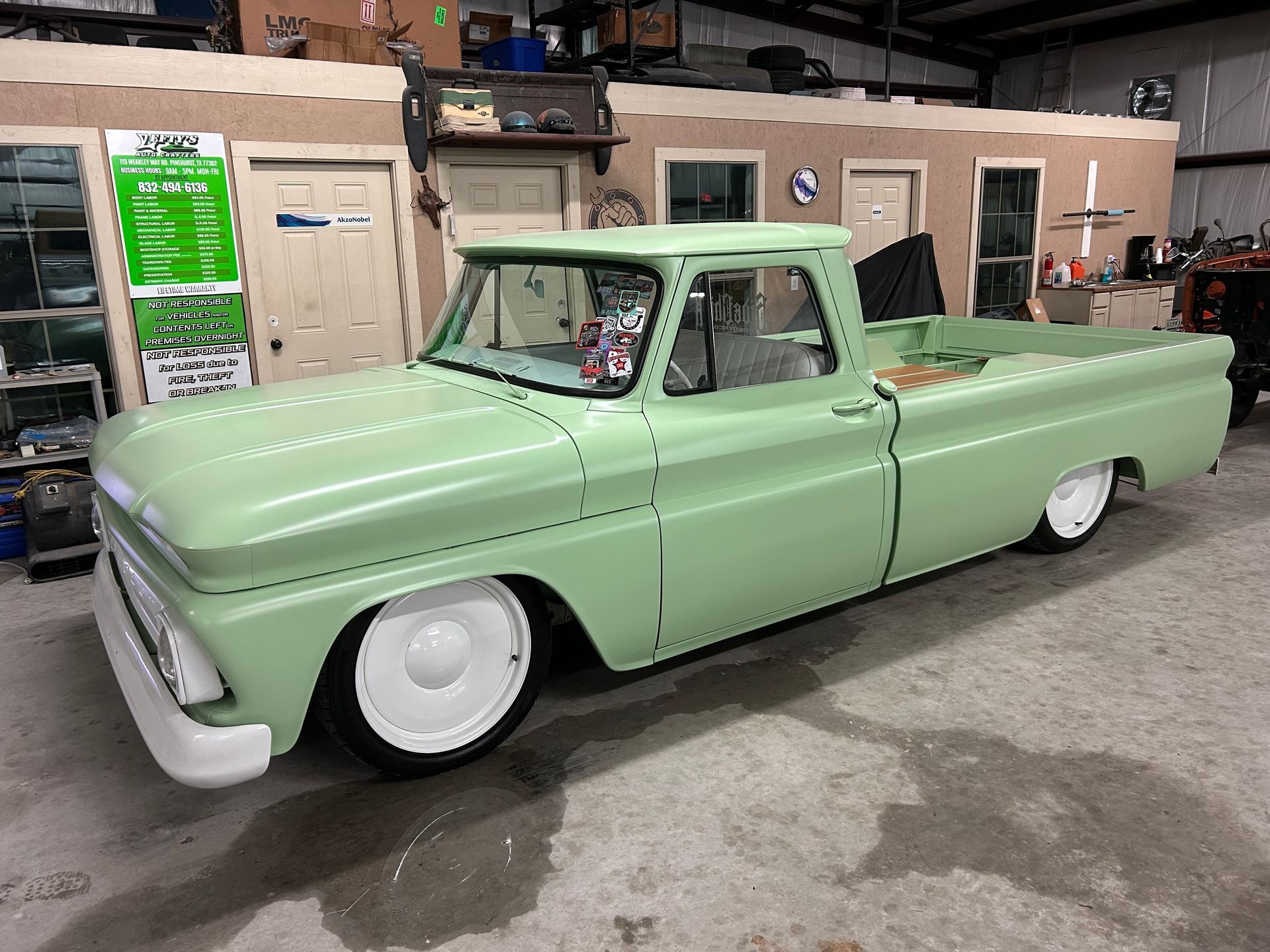 Light green classic pickup truck with white wheels in a garage.
