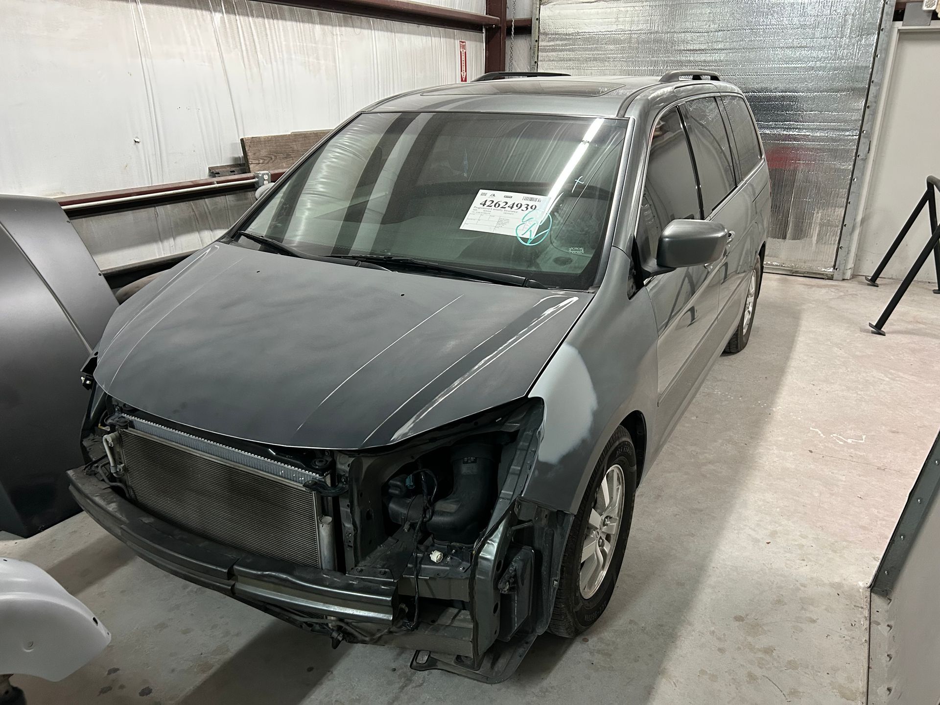 Gray minivan undergoing repairs in a workshop; front bumper removed.