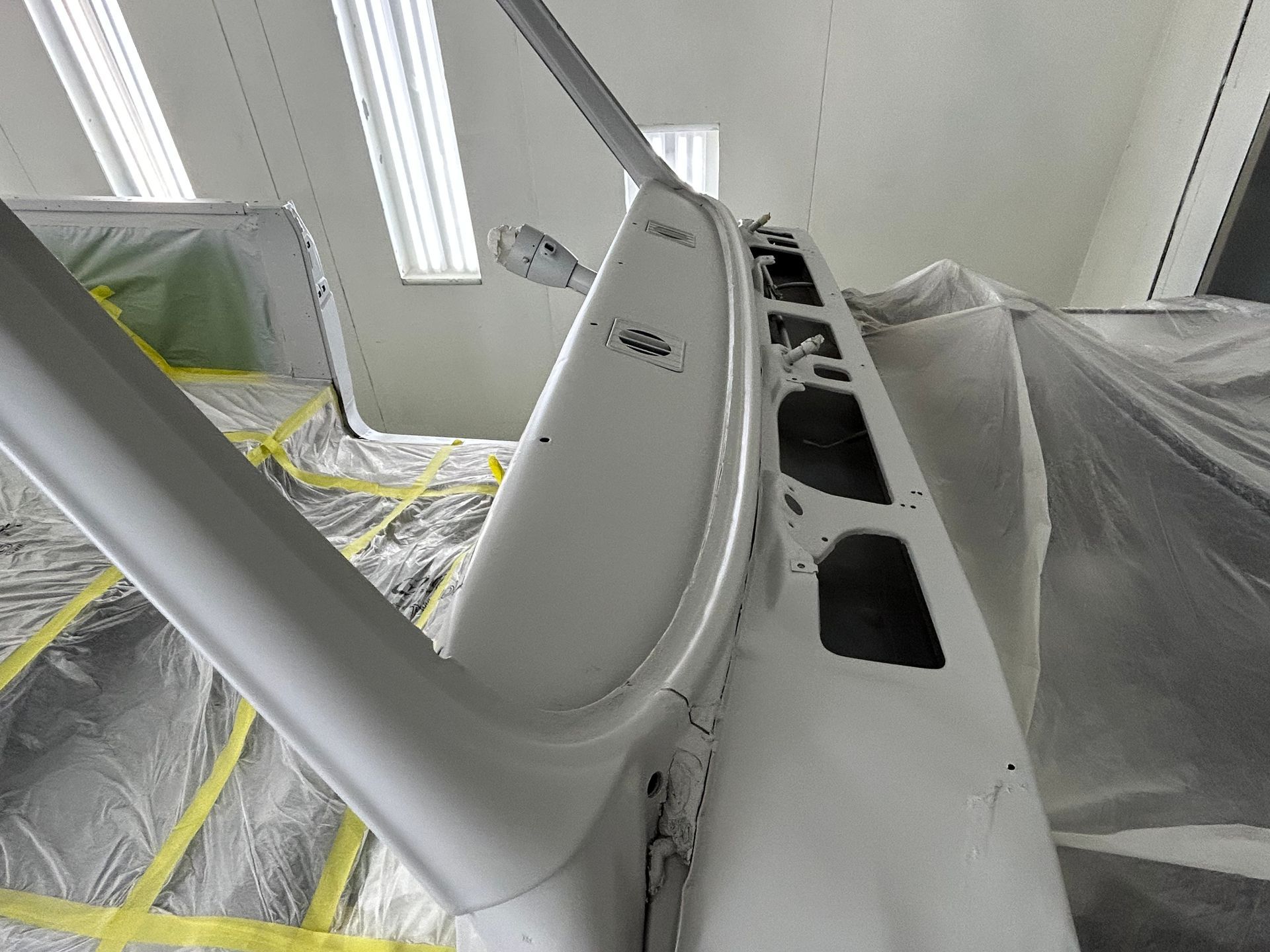 White car frame, masked for paint in a garage. Interior panel detail.