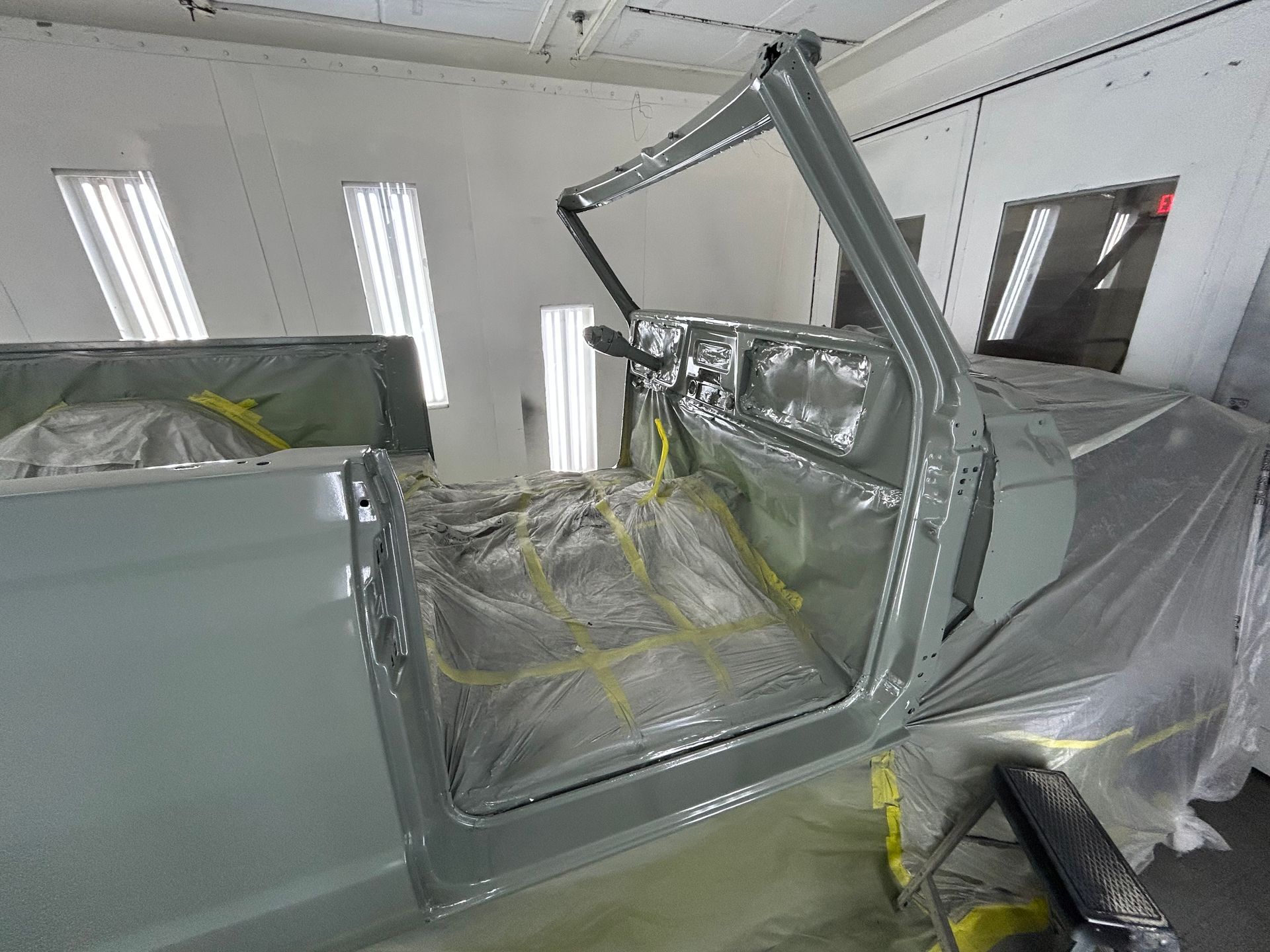 Car interior being painted light gray in a spray booth; door open.
