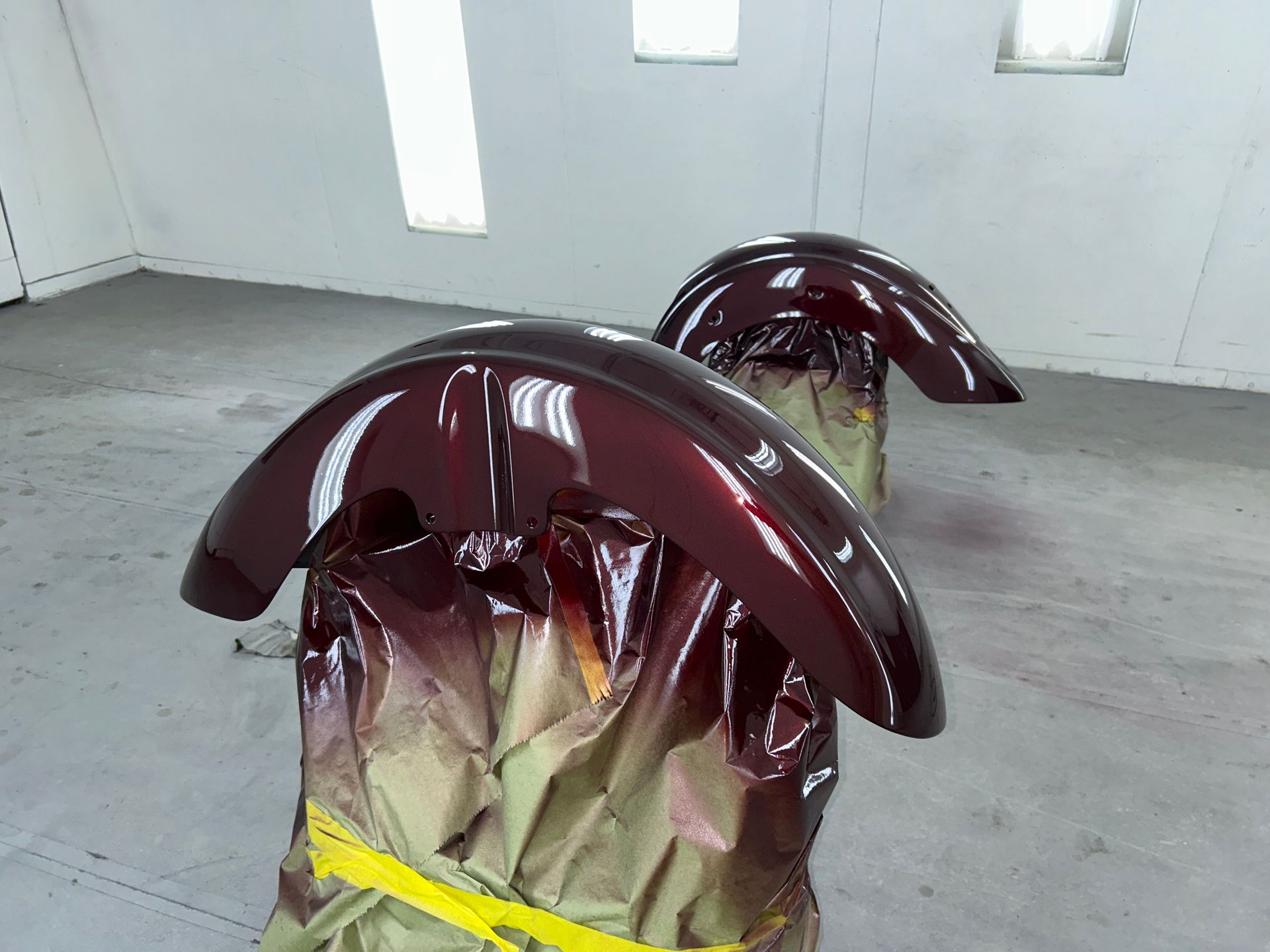 Two burgundy motorcycle fenders in a paint booth, freshly painted and drying.