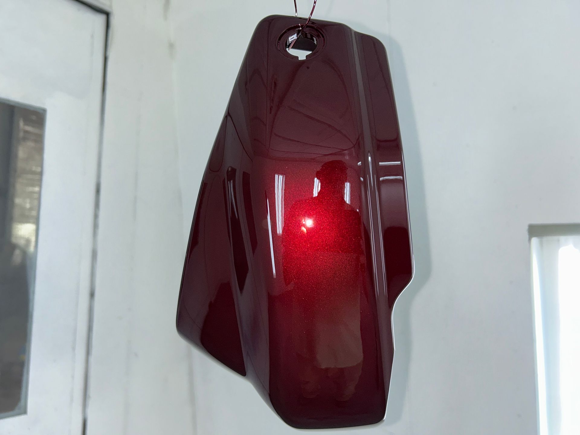 A maroon-colored motorcycle fairing suspended in a well-lit room; has a glossy, reflective surface.