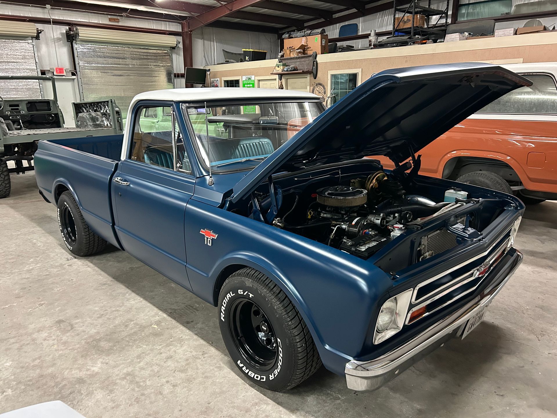 Blue and white classic Chevrolet pickup truck with hood open in a garage.