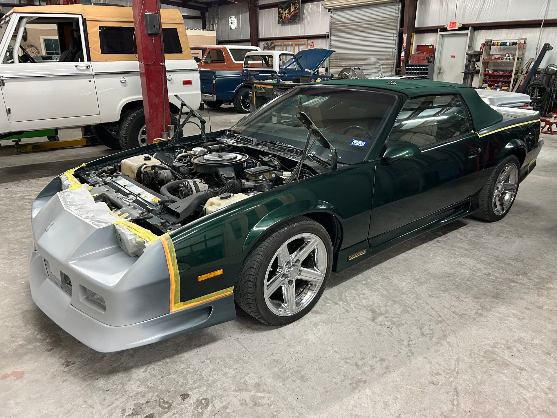 Green convertible Camaro undergoing repair in a garage.