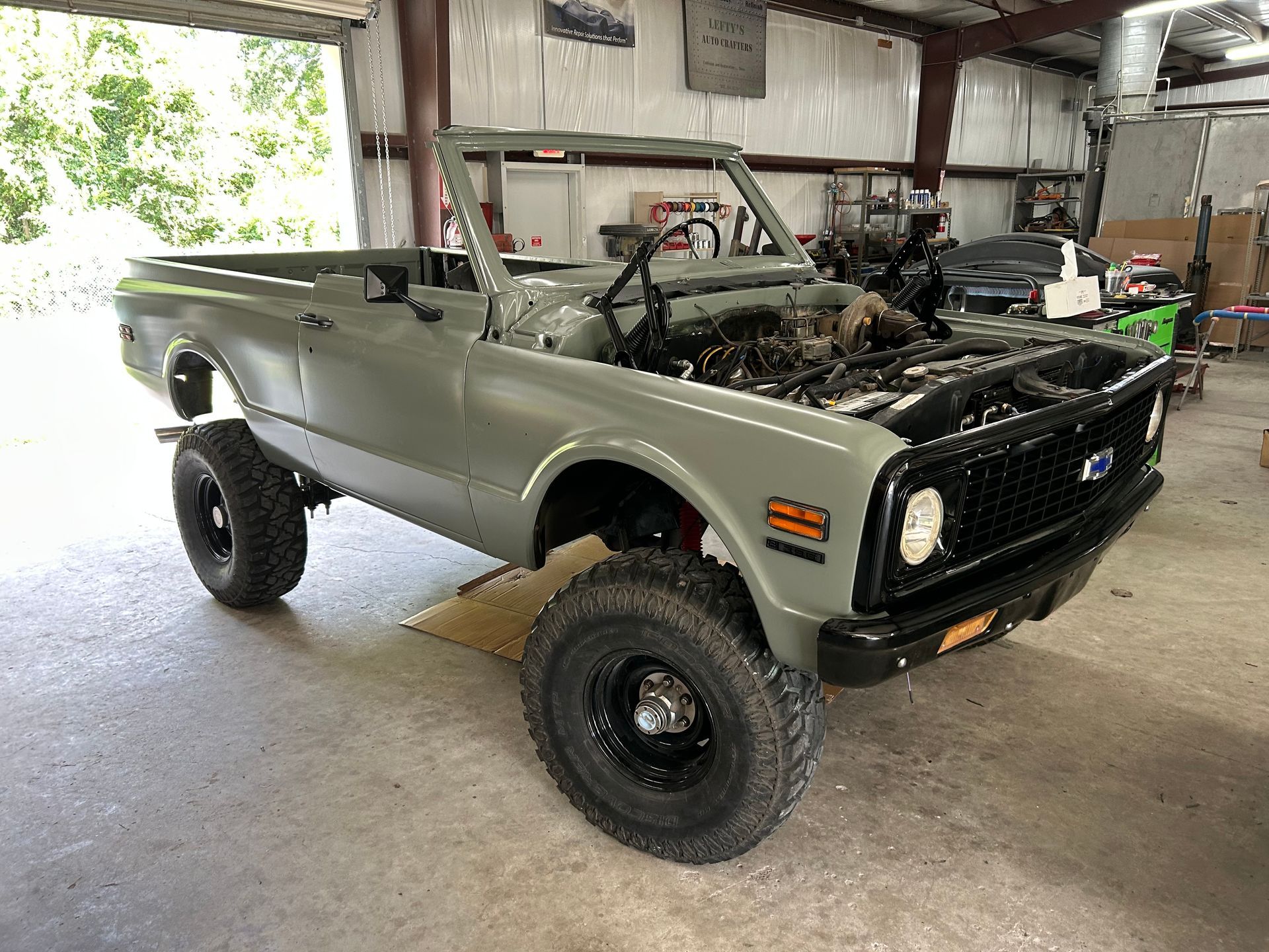 Restored vintage Chevrolet Blazer SUV, sage green, in a garage. Black wheels, open top.