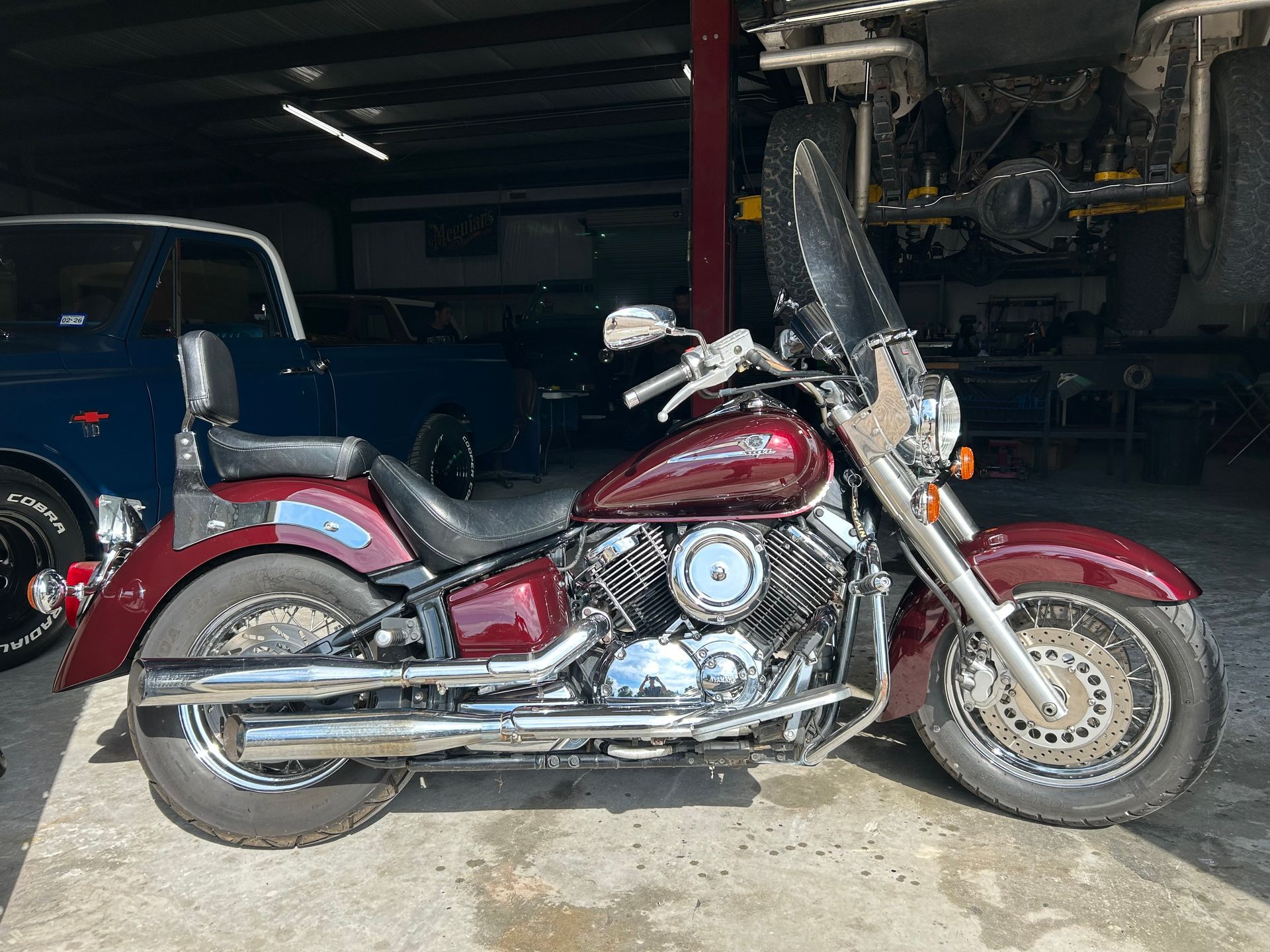 Red motorcycle in a garage, chrome accents, windshield, dark blue car in background.