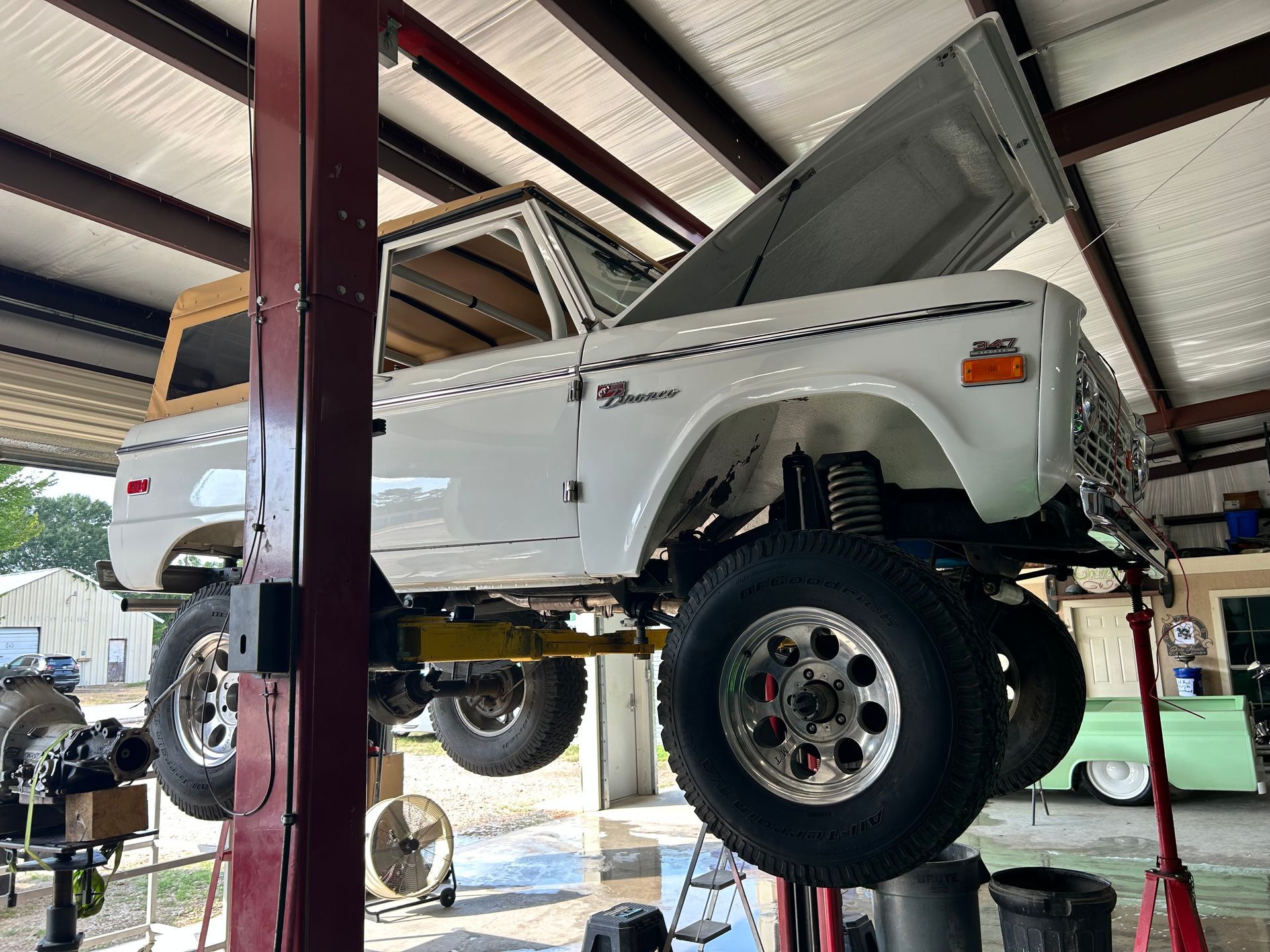 White Ford Bronco on a lift with hood open in a garage.