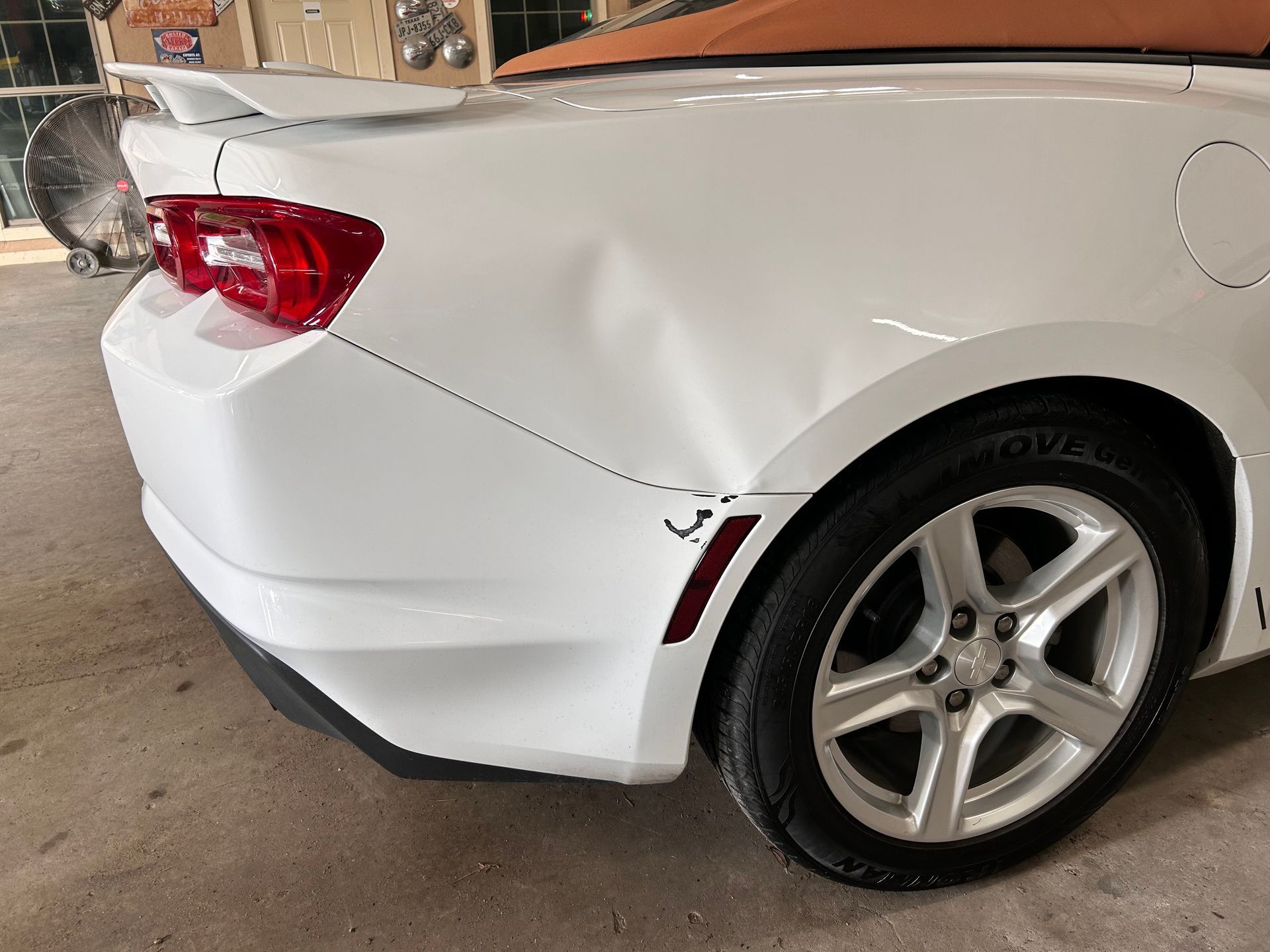 White convertible car with a dented rear quarter panel.
