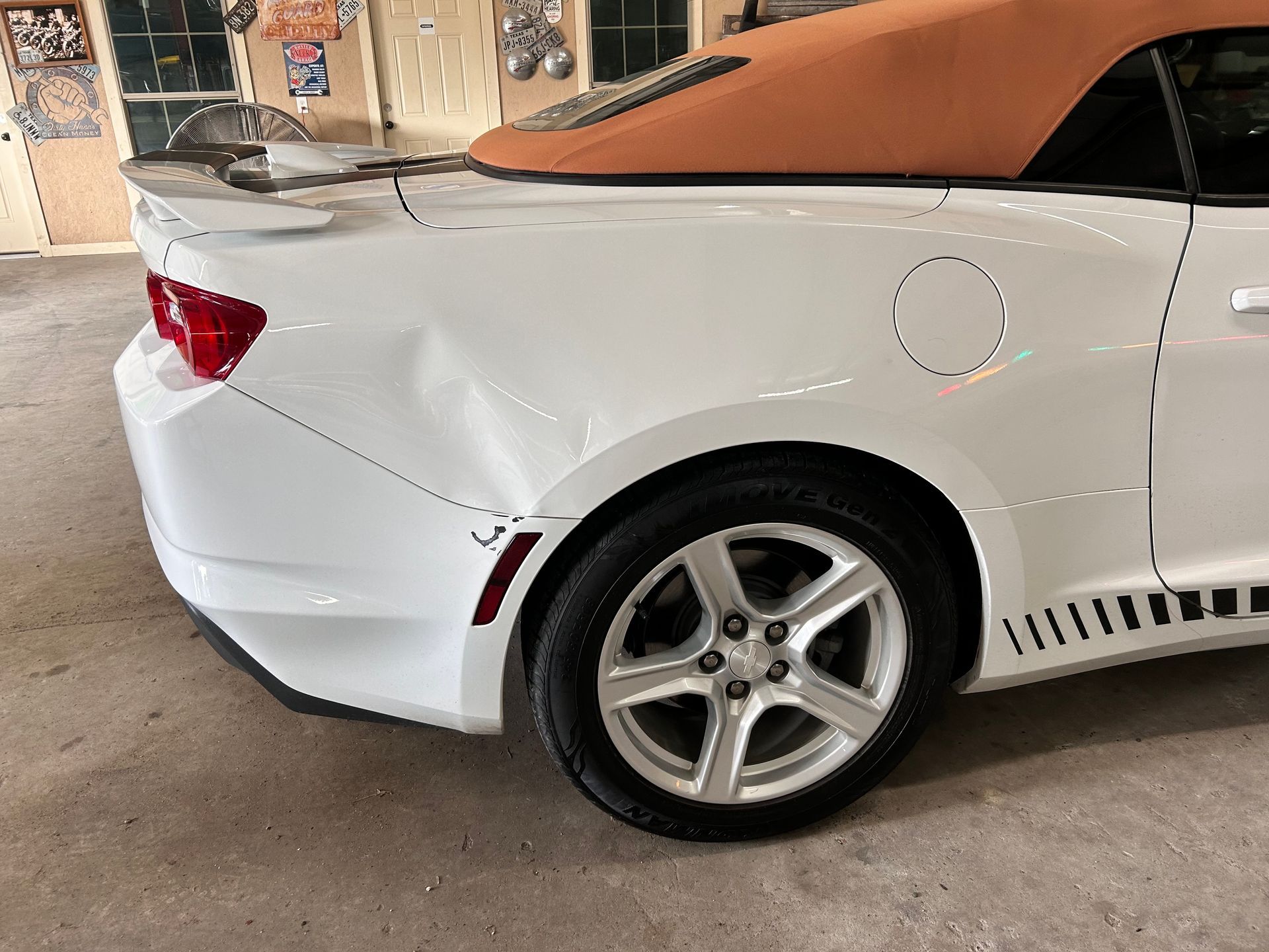 White convertible car with dent in rear quarter panel, parked indoors.