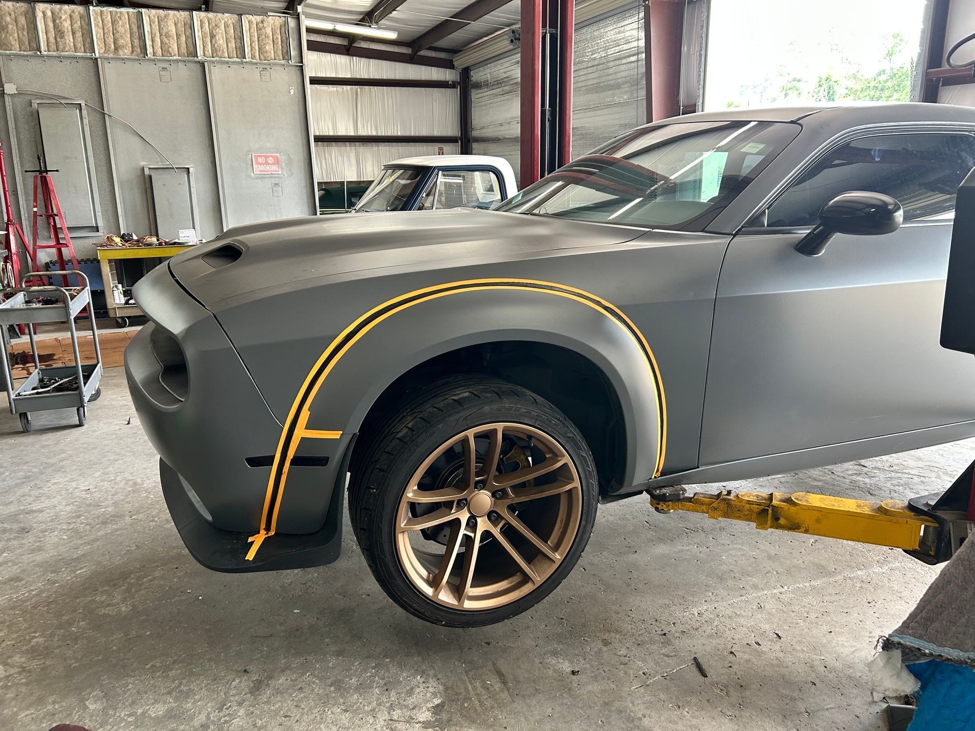 Gray Dodge Challenger on a lift, with gold accents in a garage.