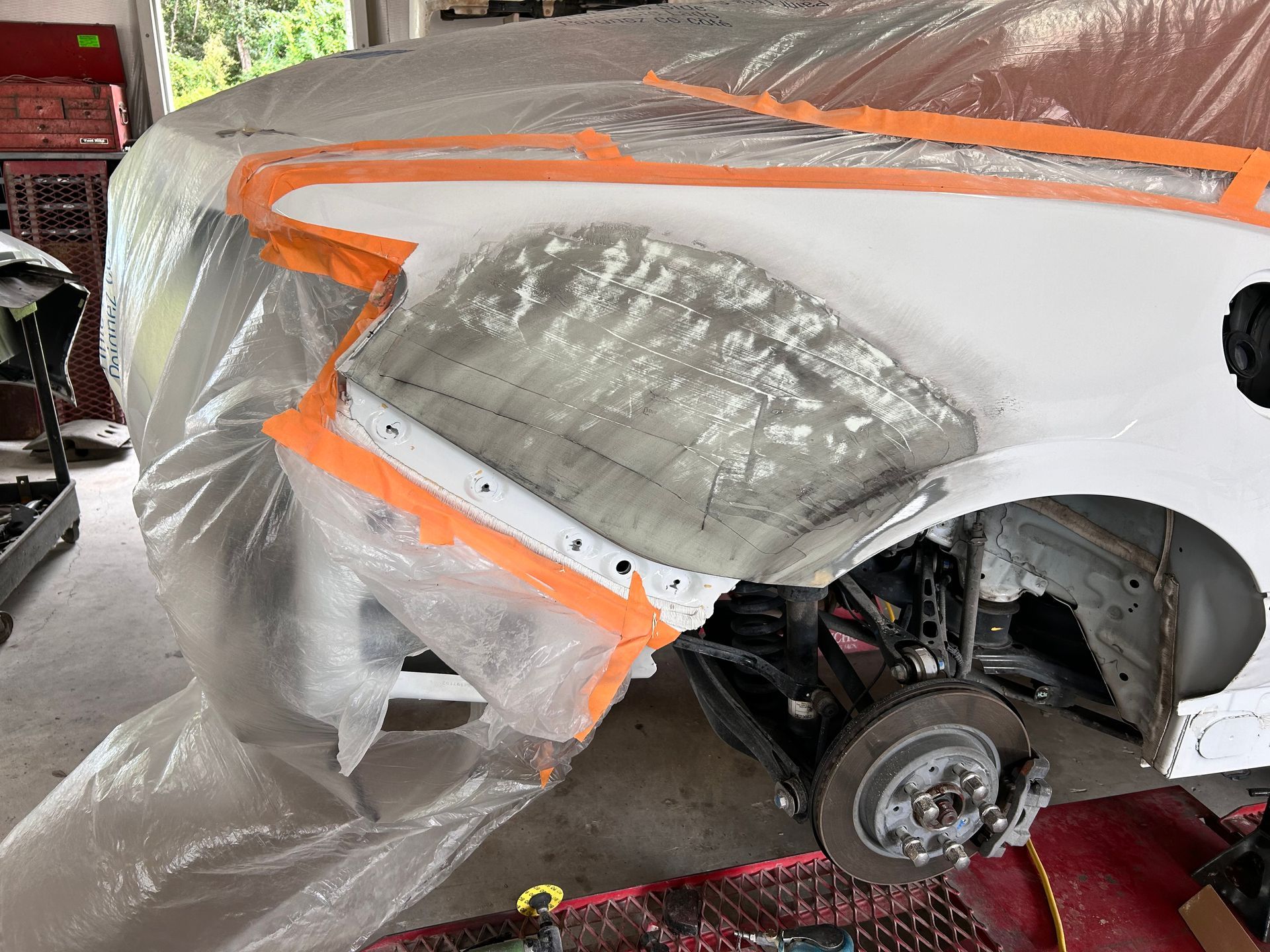 Car fender repair: White car, taped for painting, with visible primer and bodywork near wheel.
