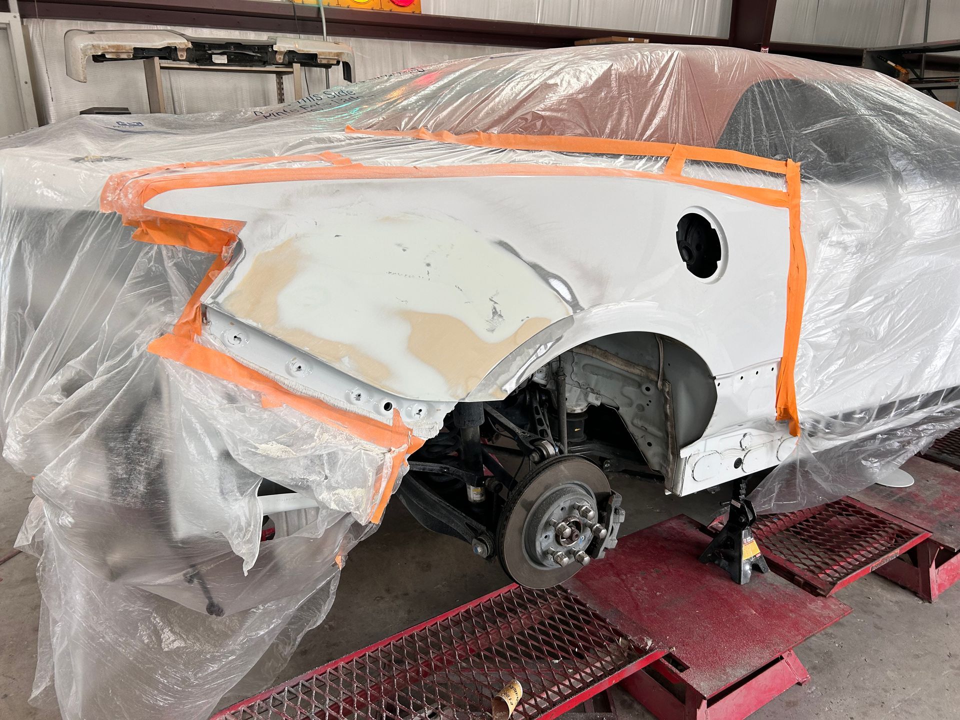 Car's rear quarter panel being repaired in a shop; covered in plastic wrap, taped, and primed for paint.