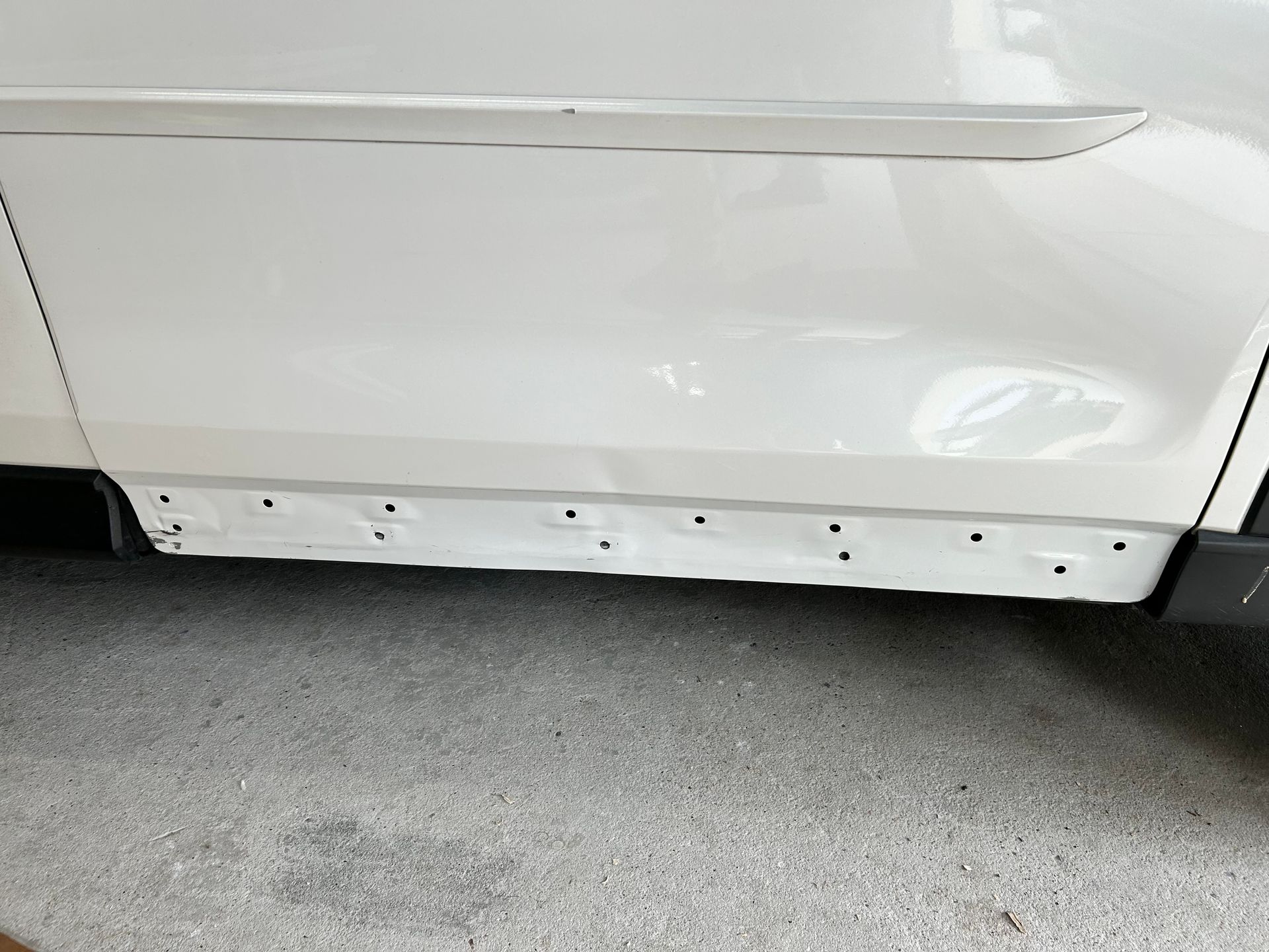 White car side panel with holes along the bottom edge, possibly for trim attachment.