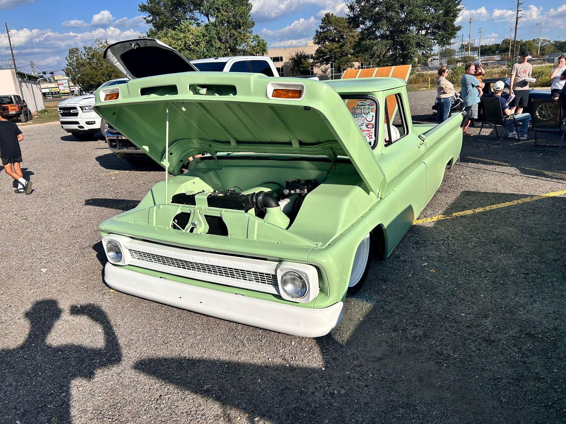 Green vintage pickup truck with hood open at an outdoor car show.
