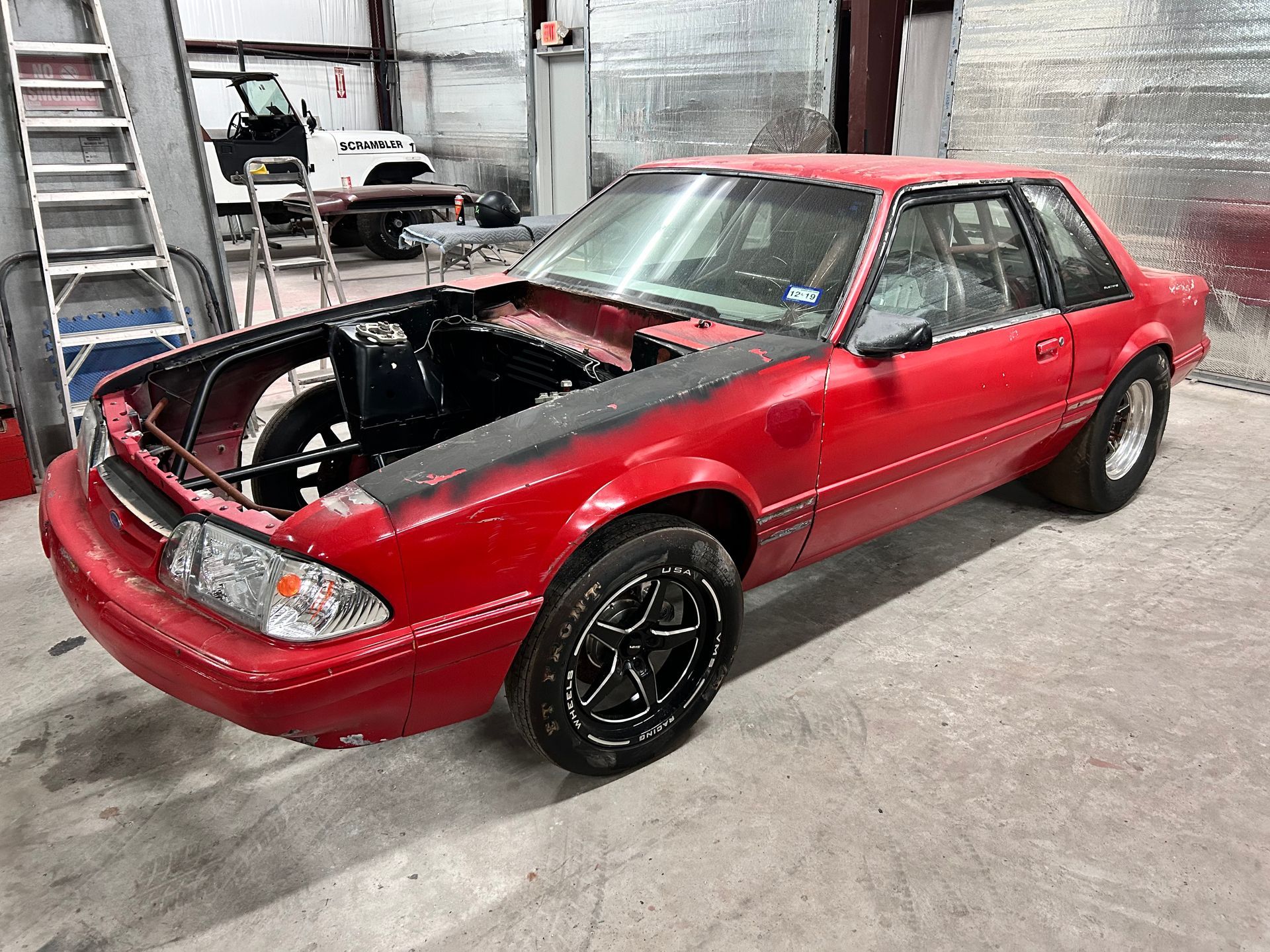 Red Ford Mustang coupe in a garage, hood open, black rims.