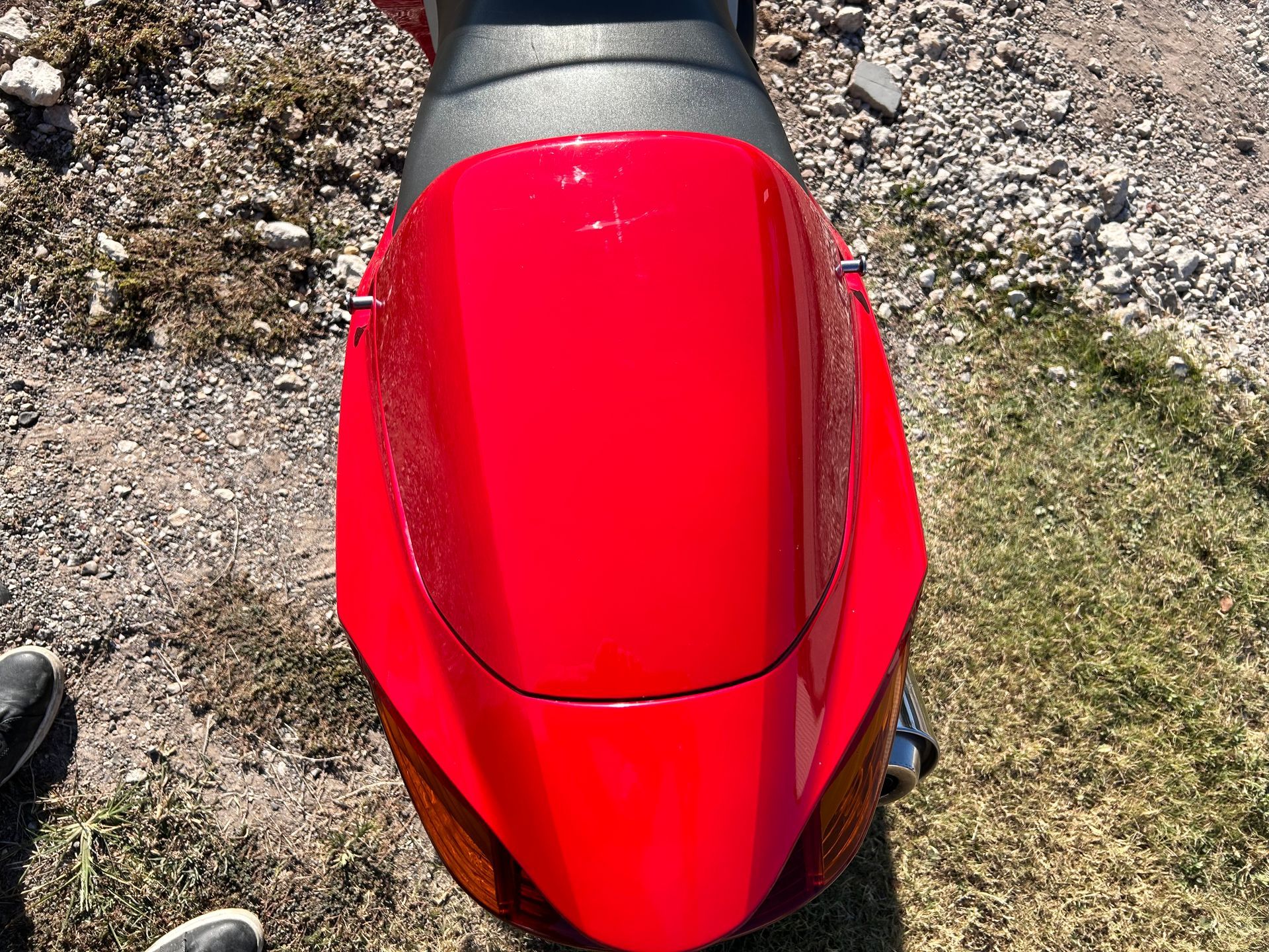 Red scooter viewed from above, parked on dirt and grass.
